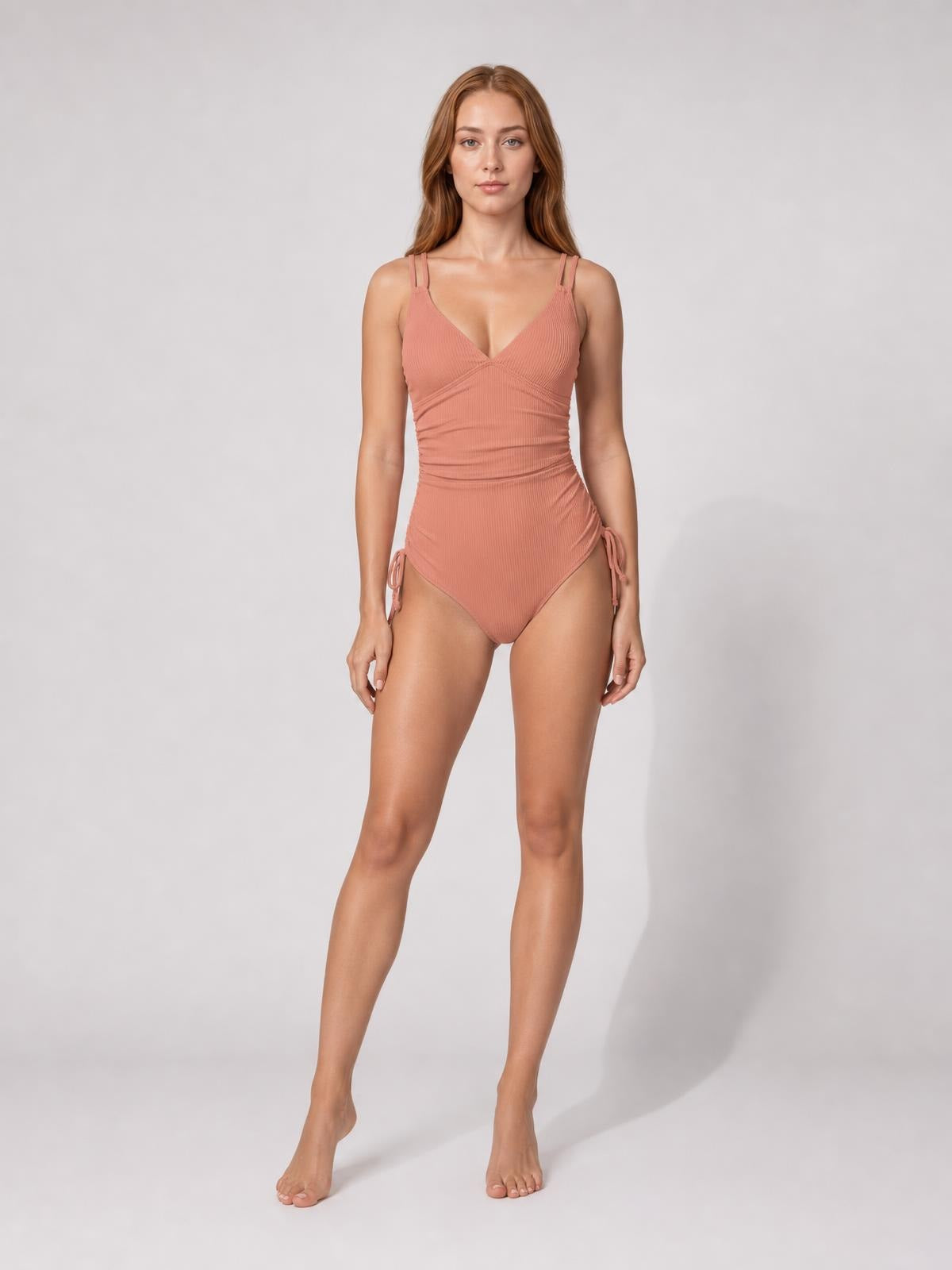 Standing model wears a solid dusty-rose tied cutout one-piece swimsuit with a plunging neckline, double shoulder straps, ruched waist, and side ties for a fitted silhouette.