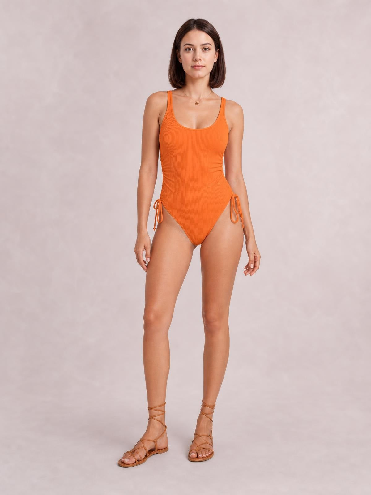 Front-facing model wears an orange tied cutout one-piece swimsuit with wide straps, a low neckline, side ties, and a fitted silhouette.