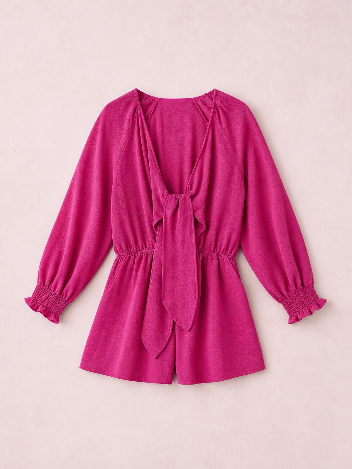 Bright fuchsia solid romper with a plunging neckline, front tie, long lantern sleeves, flounce cuffs, elastic waist, and short-leg silhouette.