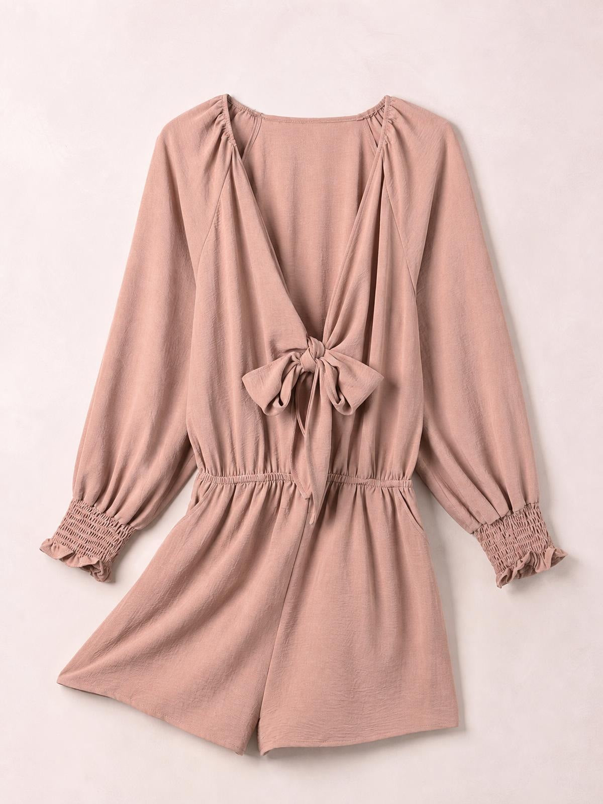 Dusty rose solid romper with a deep plunge neckline, front tie, long lantern sleeves, ruffled cuffs, elastic waist, and relaxed short-leg silhouette.