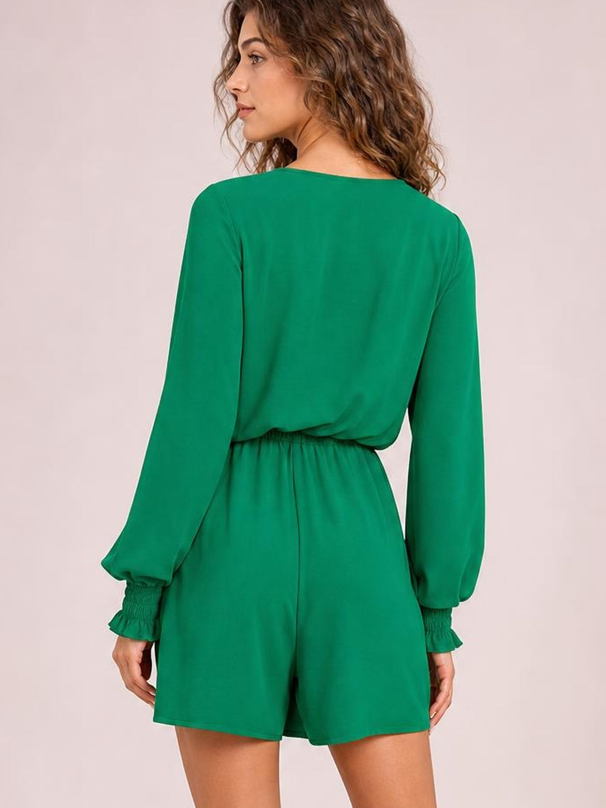 Model poses turned away in a solid green romper with a relaxed short silhouette, long lantern sleeves, elastic waist, and flounce cuffs.