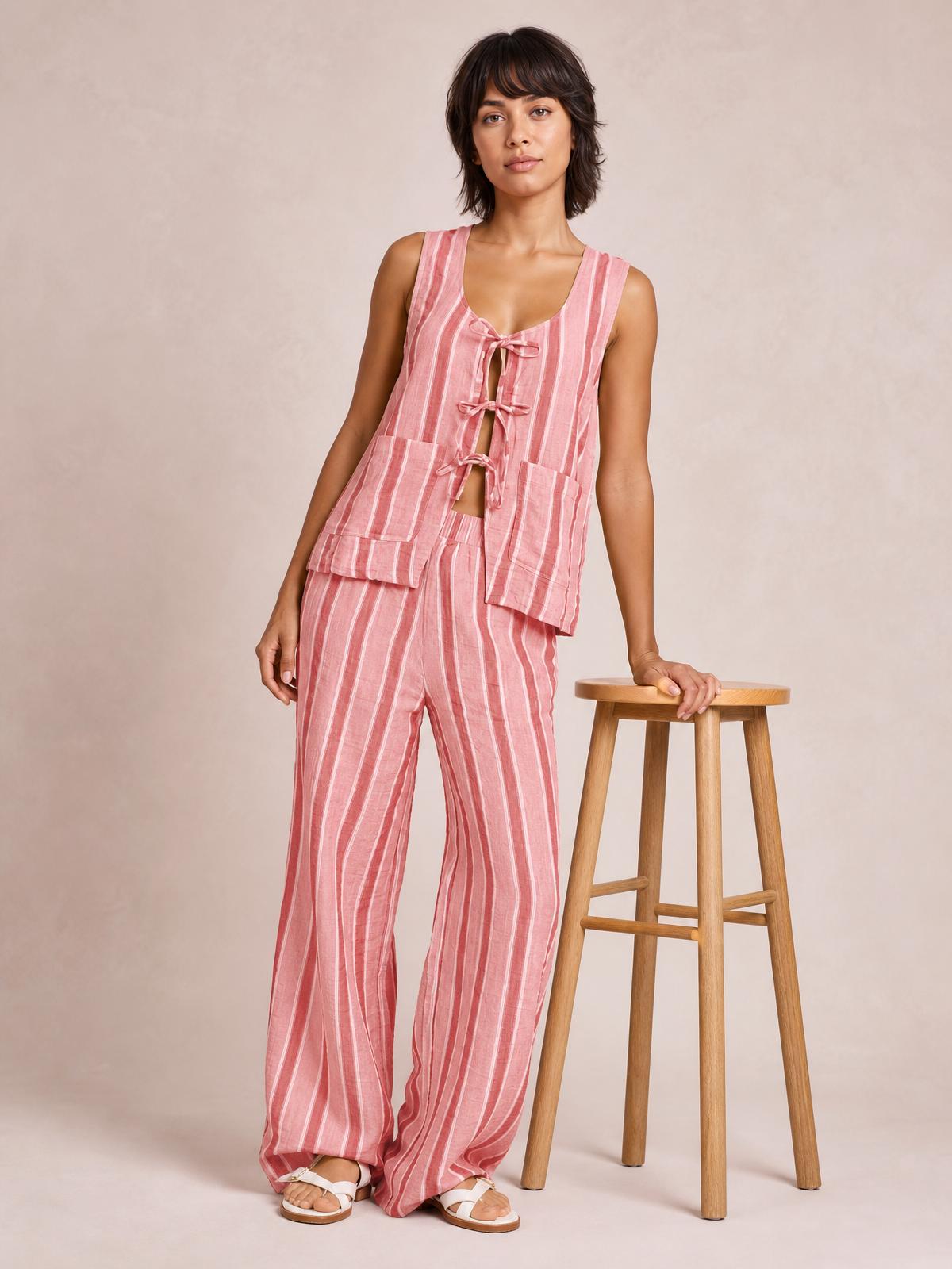 A model poses in a pink-and-white tied-front striped top and pants set with sleeveless cutout styling, pocketed panels, and relaxed wide-leg pants.