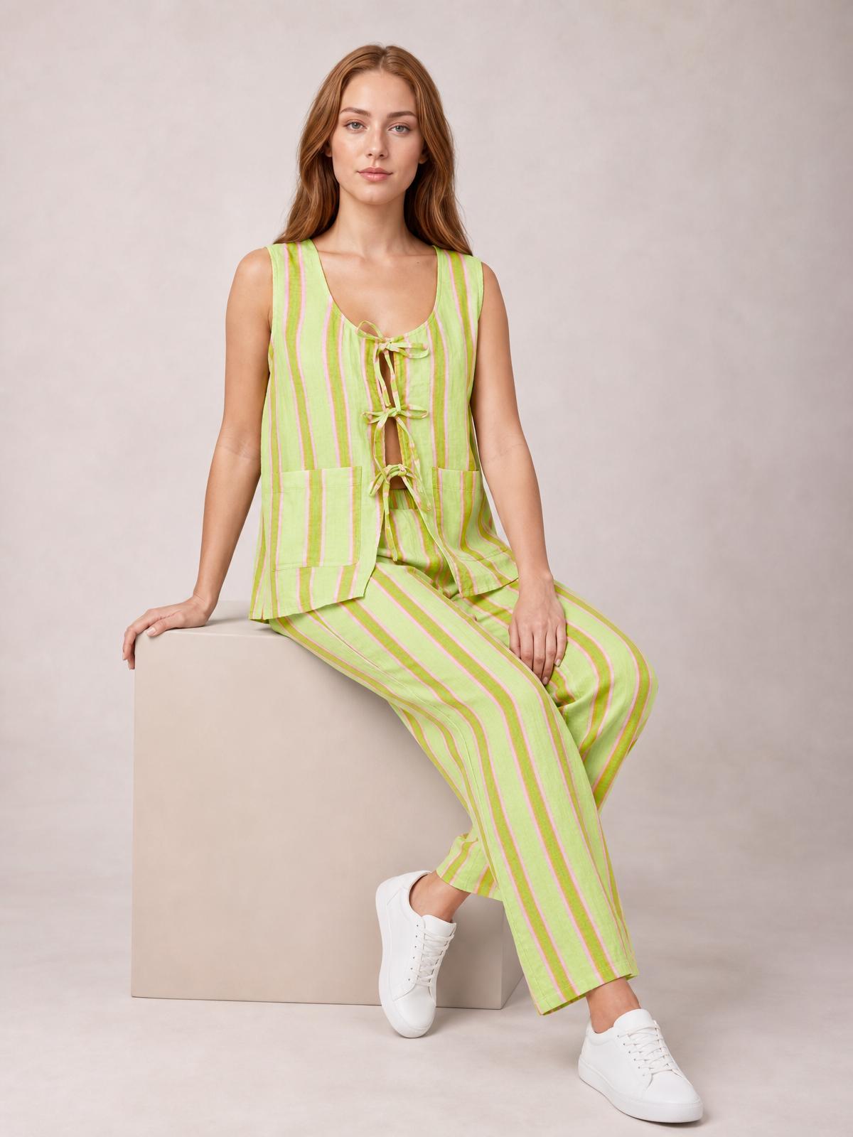 A seated model wears a lime green and pink striped top with sleeveless styling, tied front, patch pockets, and matching wide-leg pants.