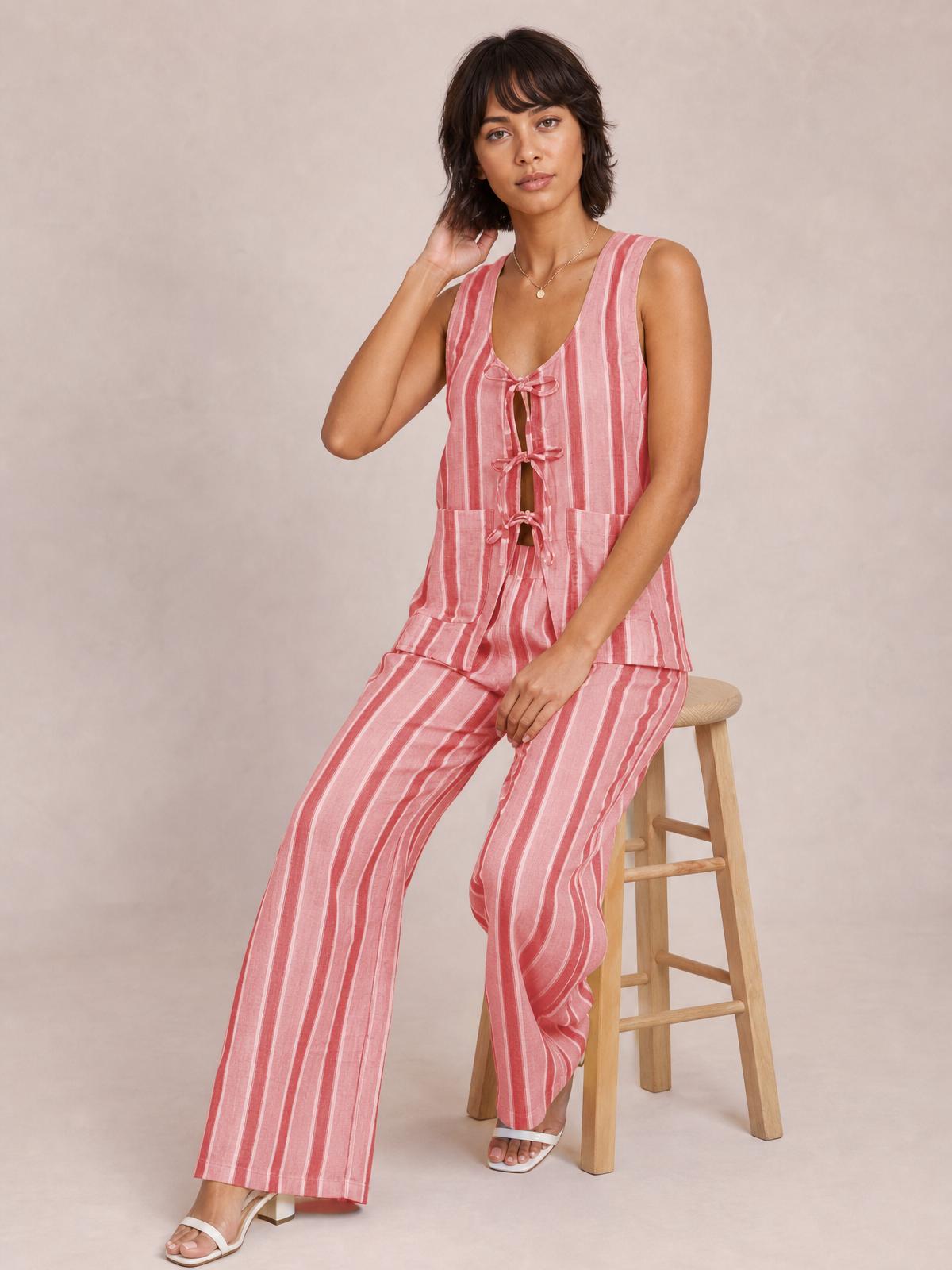 Model seated in a pink striped set with a sleeveless tied-front top, multiple front ties, and matching wide-leg pants.