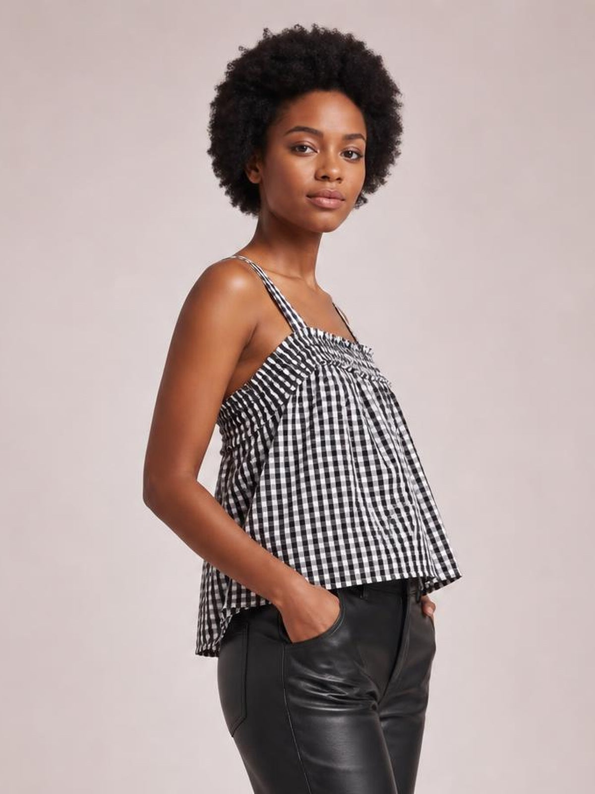 Model poses with hands in pockets wearing a black-and-white textured gingham cami with thin straps, a square neckline, and a loose flared silhouette.