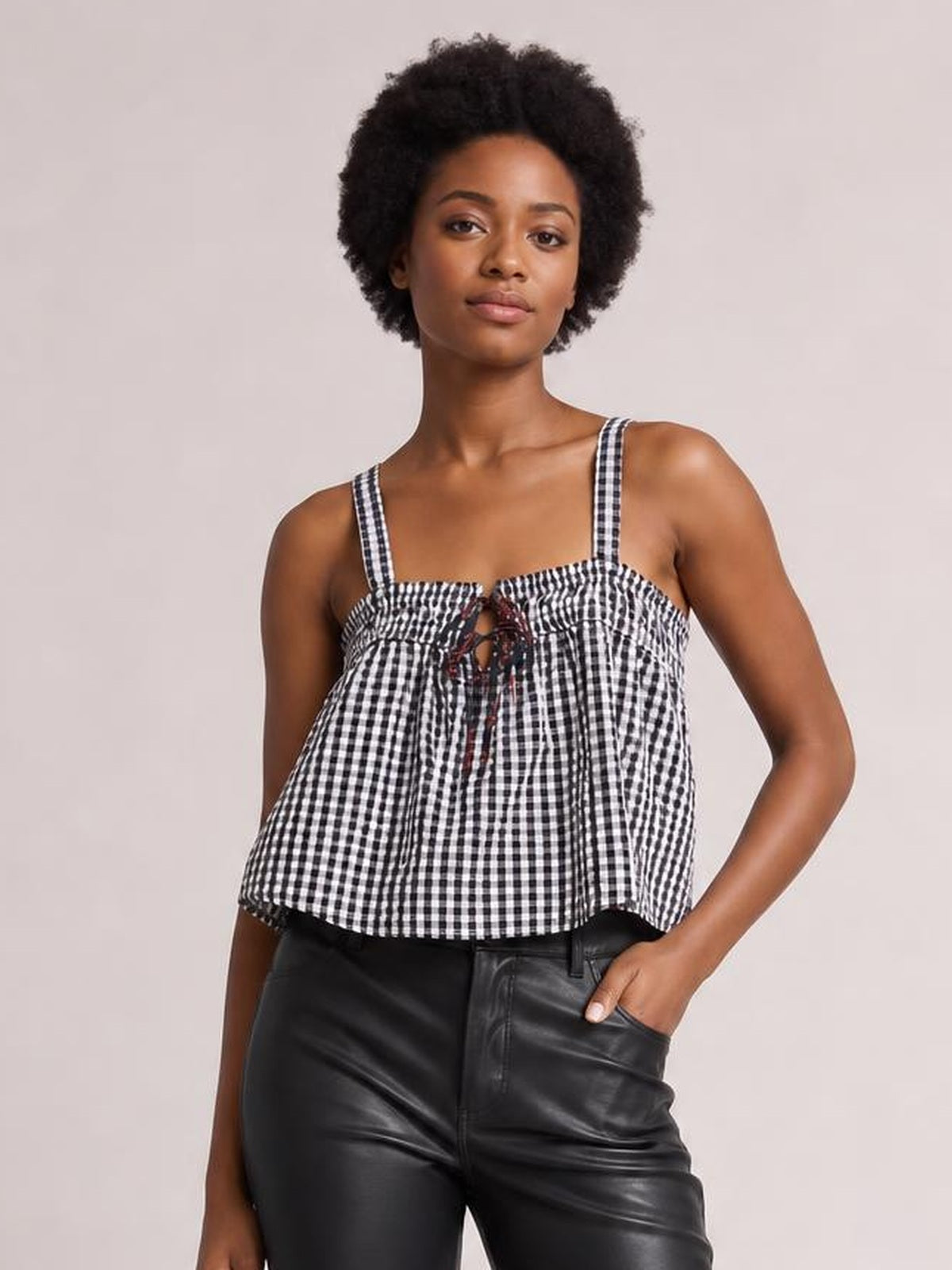 A model wears a black-and-white textured cami with a square neckline, shoulder straps, tied front detail, and a relaxed flared silhouette.