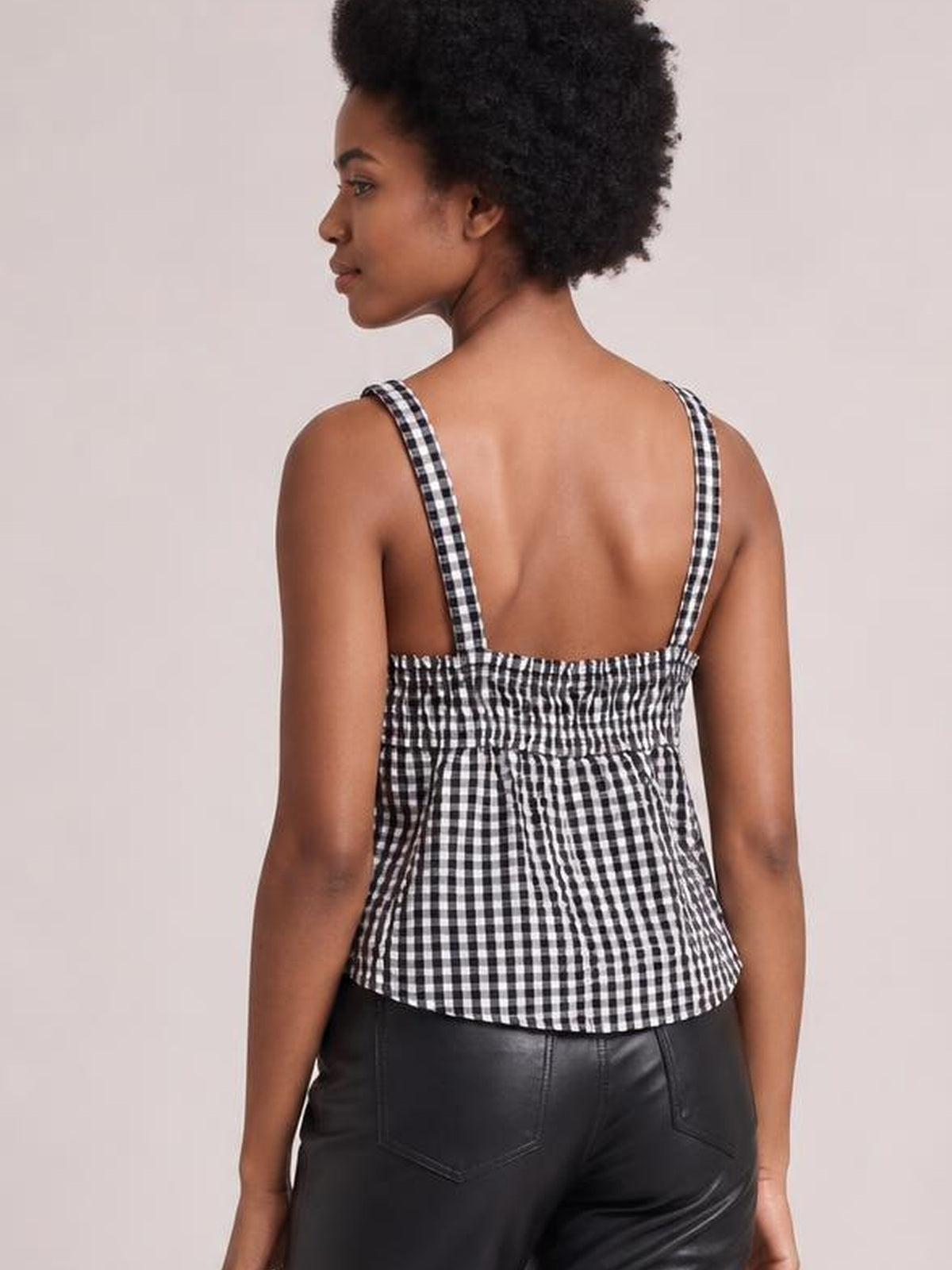 A model shown from the back wears a black-and-white textured checked cami with wide straps, a smocked back panel, and a gently flared hem.