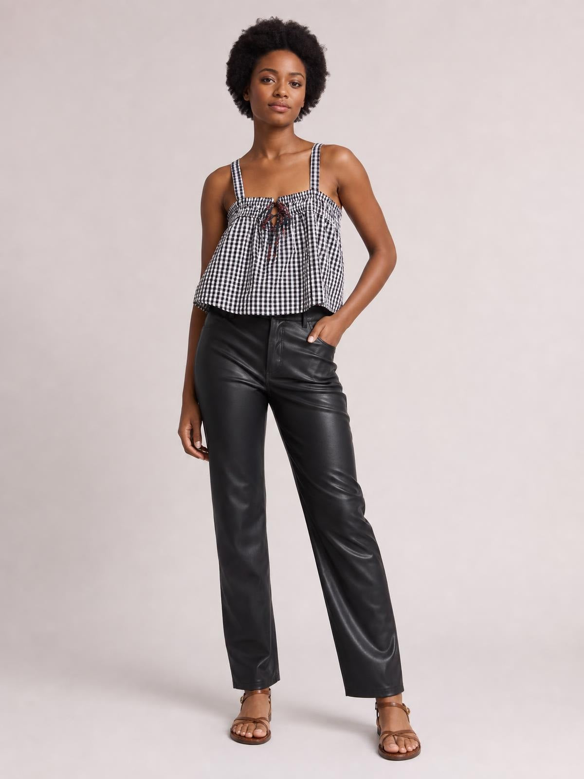 Model wears a black-and-white textured cami with a square neckline, shoulder straps, tied front, and relaxed flared silhouette, posing with one hand in her pocket.