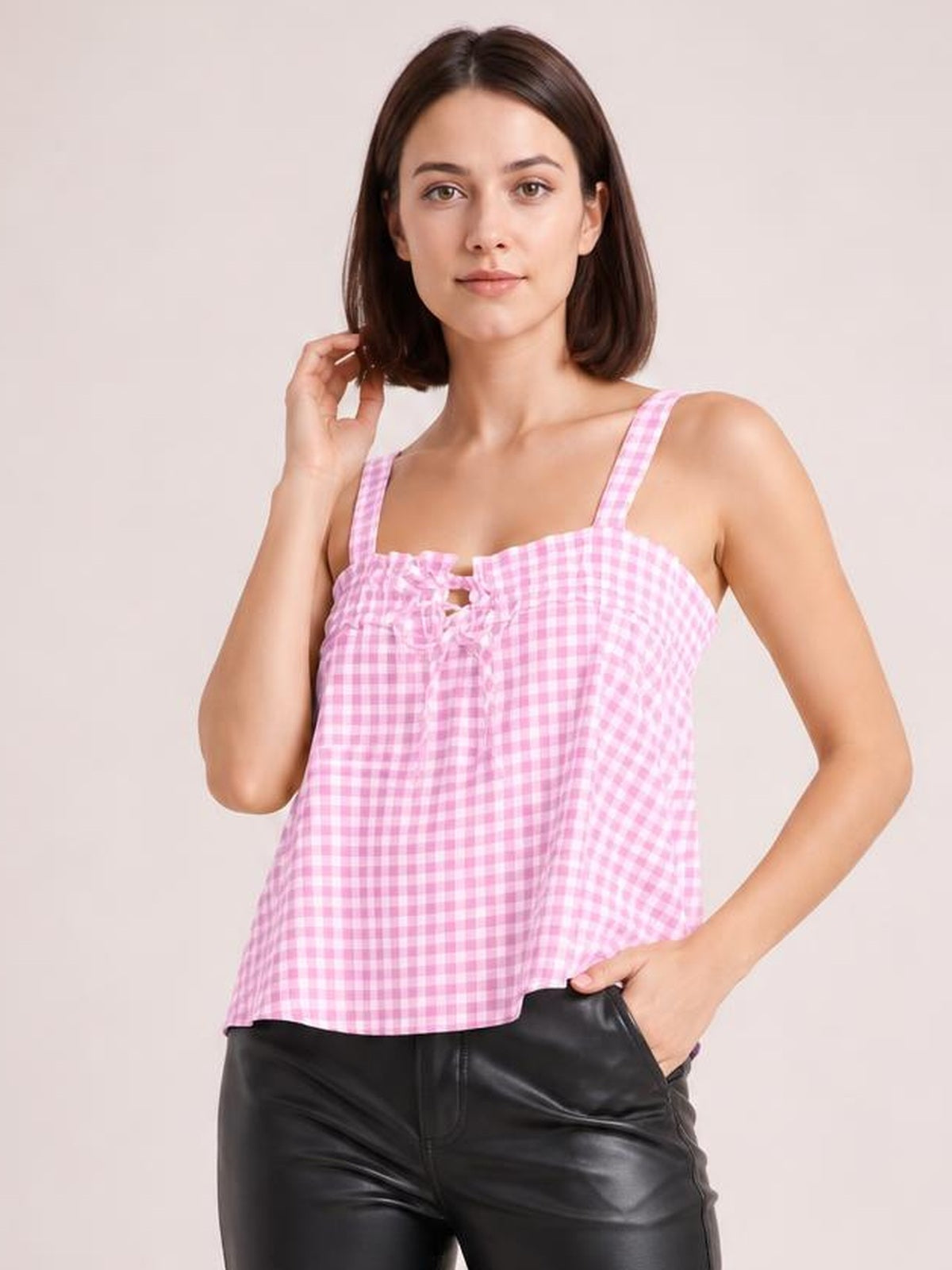 Model poses in a pink textured gingham cami with a square neckline, wide shoulder straps, tied front detail, and a relaxed cropped silhouette.