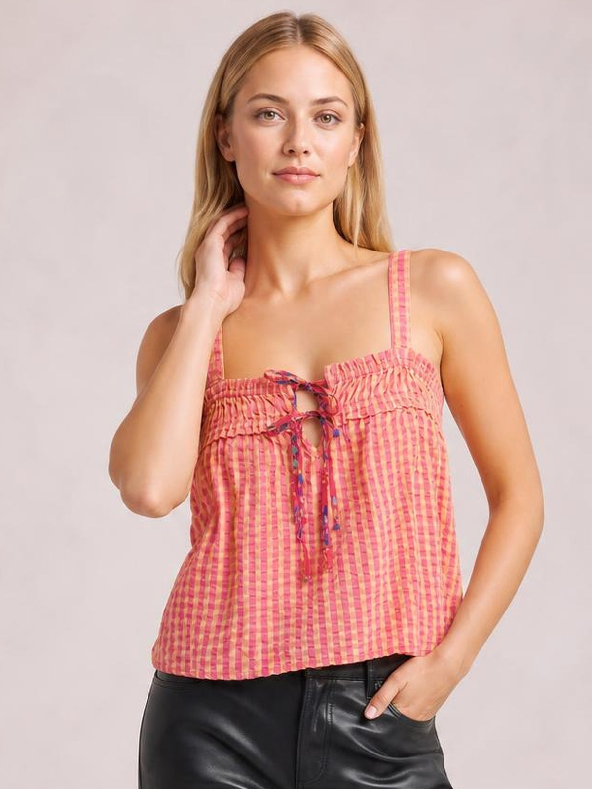 A model poses in a pink textured square-neck cami with thin straps, a tied front with keyhole opening, ruffled detailing, and a relaxed straight silhouette.