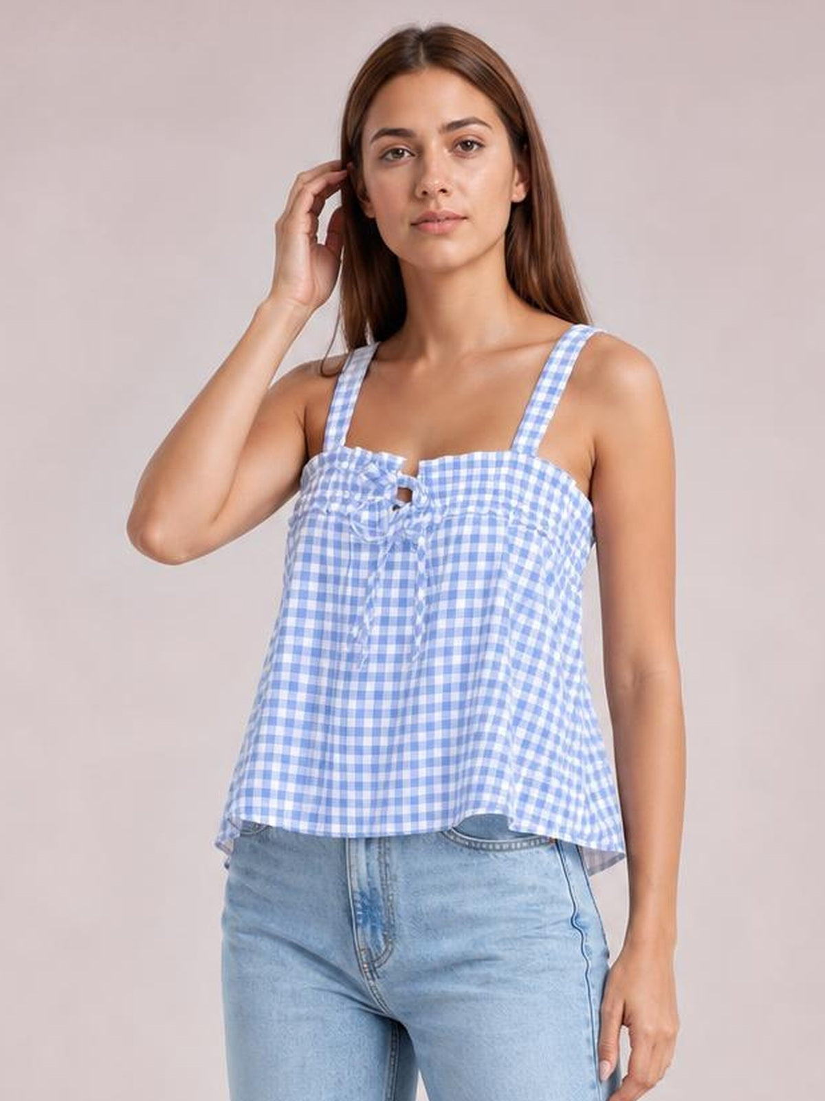 Model touching her hair wears a blue-and-white textured gingham cami with a square neckline, wide straps, tied front detail, and a loose flared silhouette.
