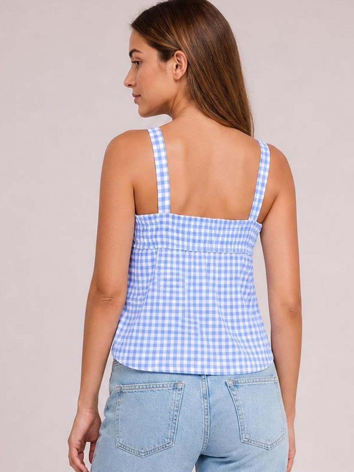 A model poses from behind in a blue-and-white textured gingham cami with thin straps, a square back neckline, and a relaxed silhouette.