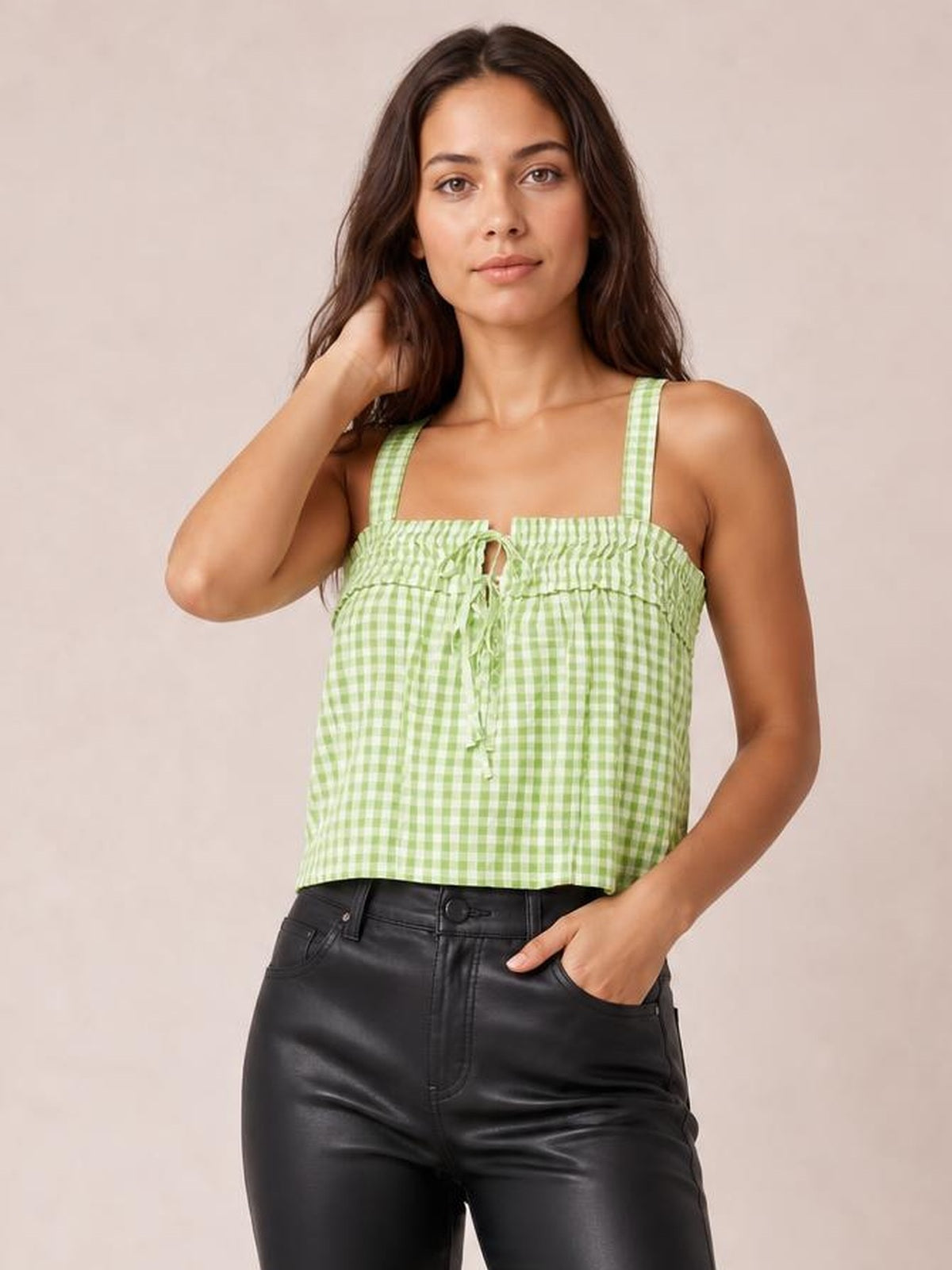 Model poses in a green gingham textured square-neck cami with wide straps, a tied front, smocked bodice, and cropped relaxed silhouette.