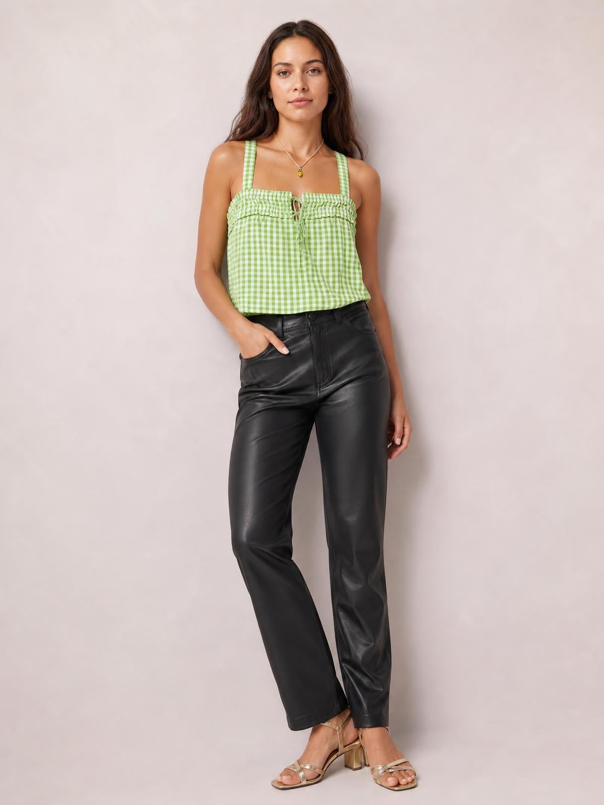 A model stands with one hand in her pocket wearing a green-and-white textured square-neck cami with wide straps, a tied front, and a relaxed silhouette.