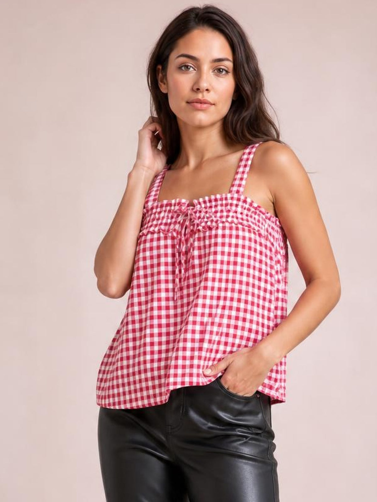 Model poses in a pink-and-white gingham cami with a textured square neckline, wide straps, tied front, and relaxed flared silhouette.