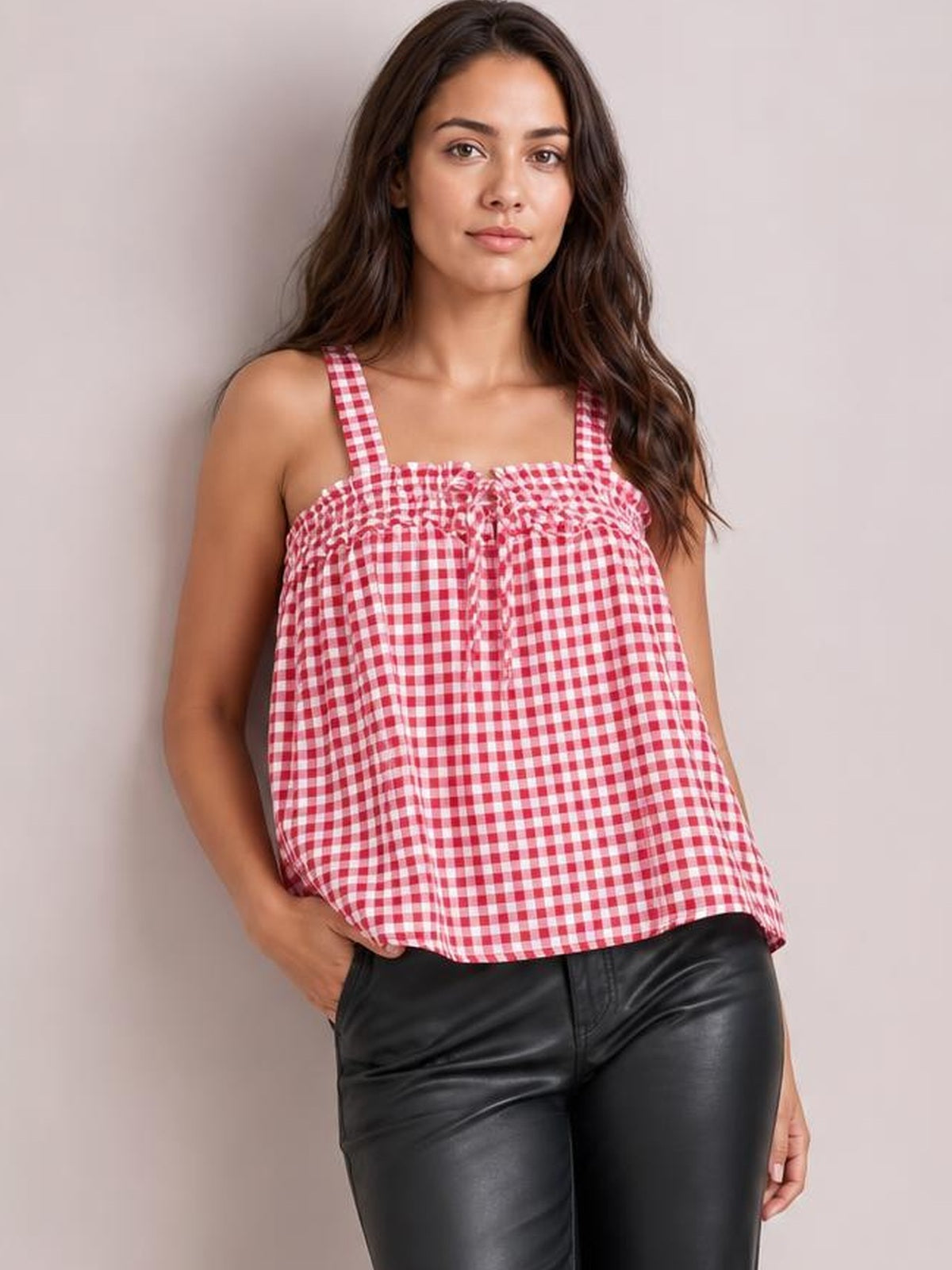 Model wears a pink-and-white gingham textured cami with a square neckline, shoulder straps, tied front detail, and relaxed A-line silhouette.