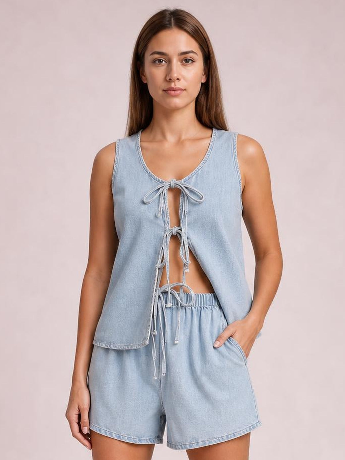 Model wearing a light-blue denim set with a sleeveless V-neck vest, tied bow-front cutouts, and relaxed high-waisted shorts with pockets.