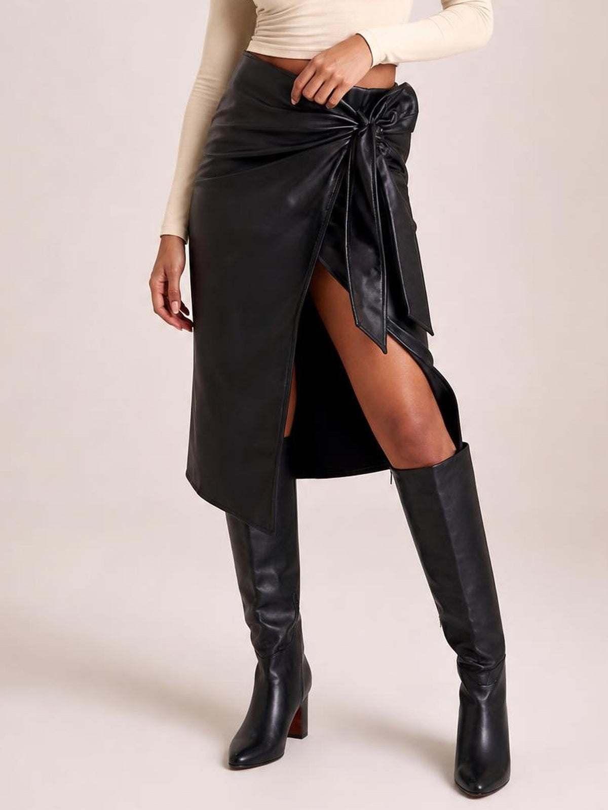 Model poses in a black high-waist skirt with a tied waist, ruched construction, fitted silhouette, and asymmetrical front slit.