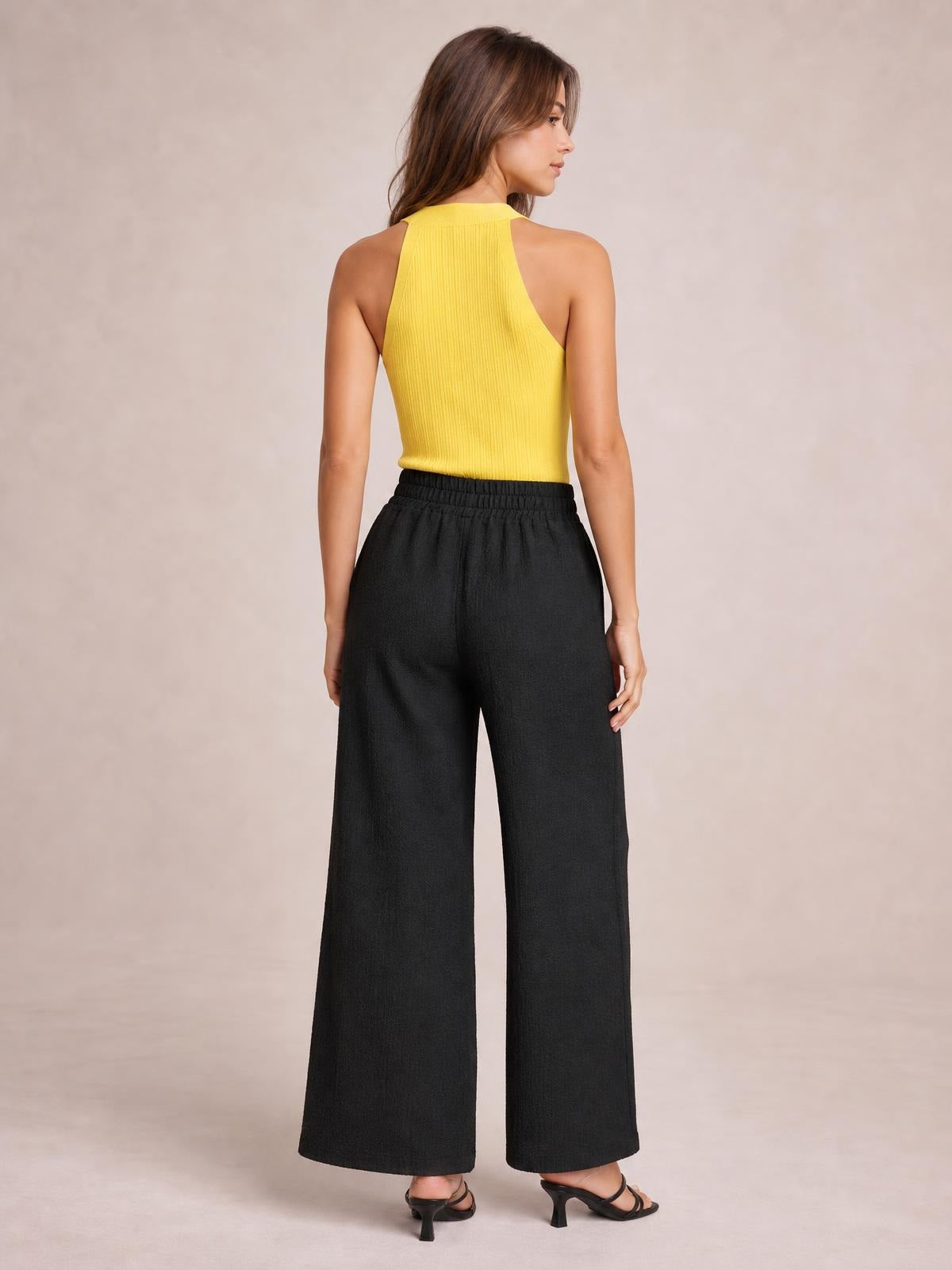 A model stands turned away in black opaque high-waist wide-leg pants with a relaxed full-length silhouette and elasticized waistband.