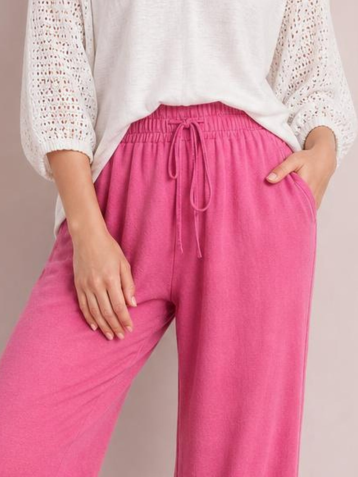 Model wearing bright pink tied high-waist wide-leg pants with a drawstring waistband and side pockets, shown with one hand in a pocket.
