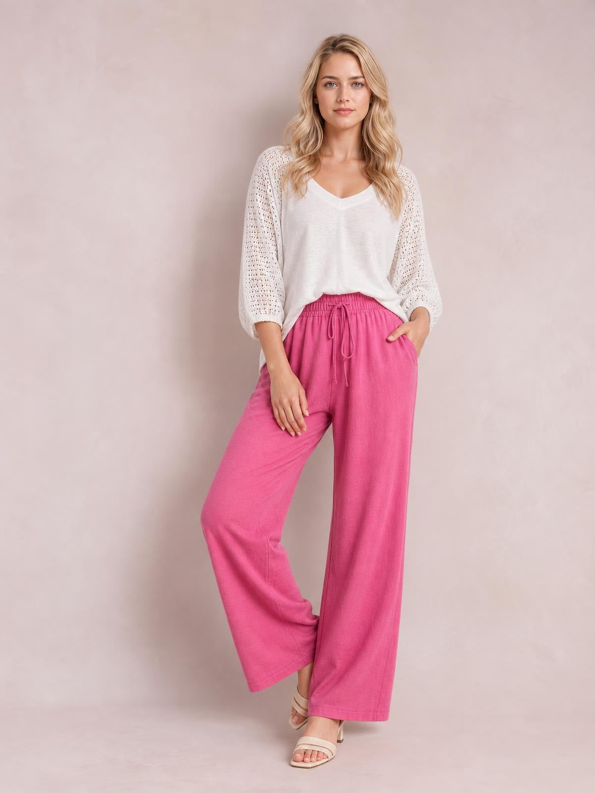 Model poses in bright pink tied high-waist wide-leg pants with a drawstring waist, relaxed silhouette, and visible side pockets.