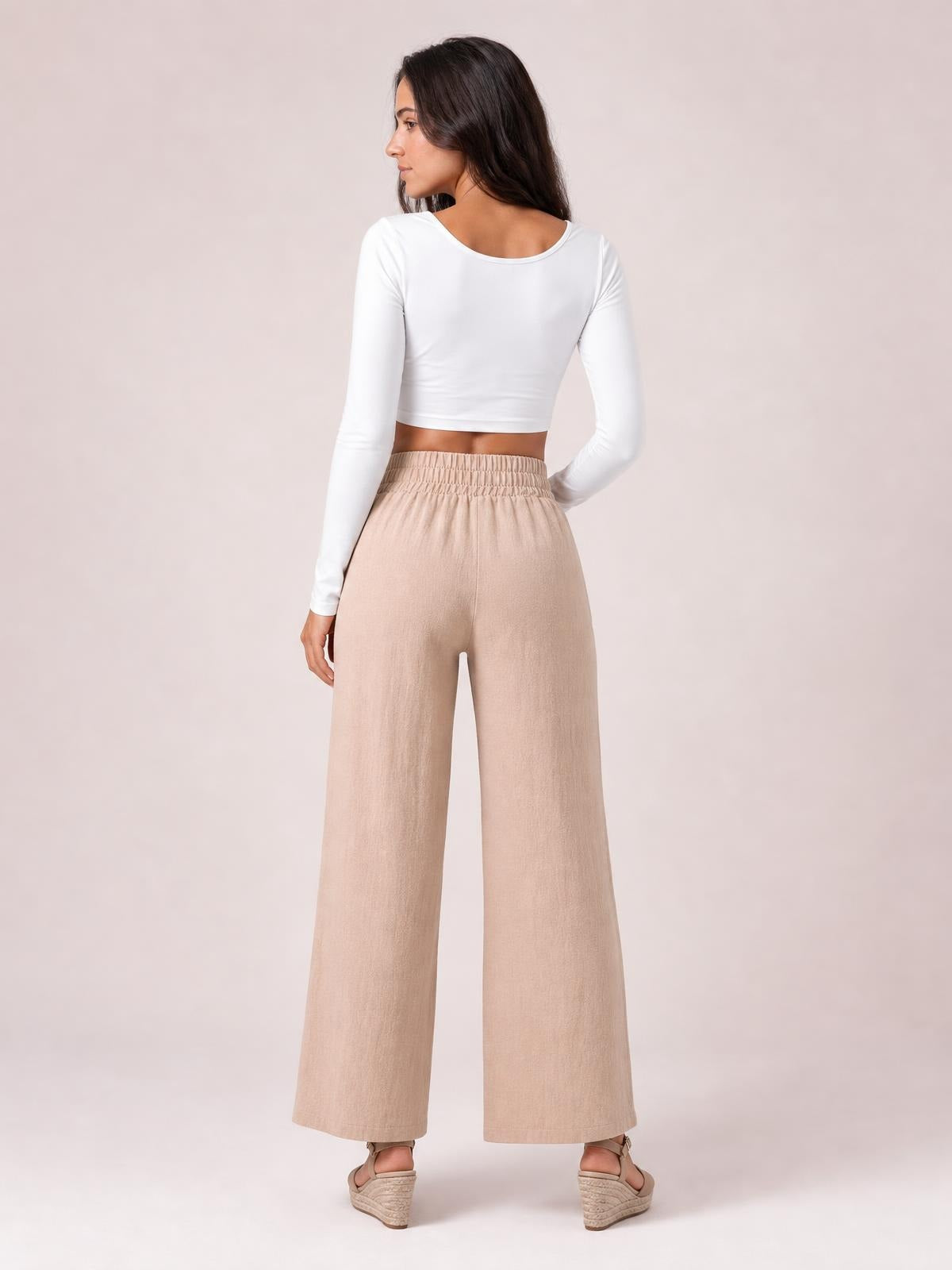A model poses from behind in opaque beige high-waist wide-leg pants with a relaxed silhouette and softly structured construction.