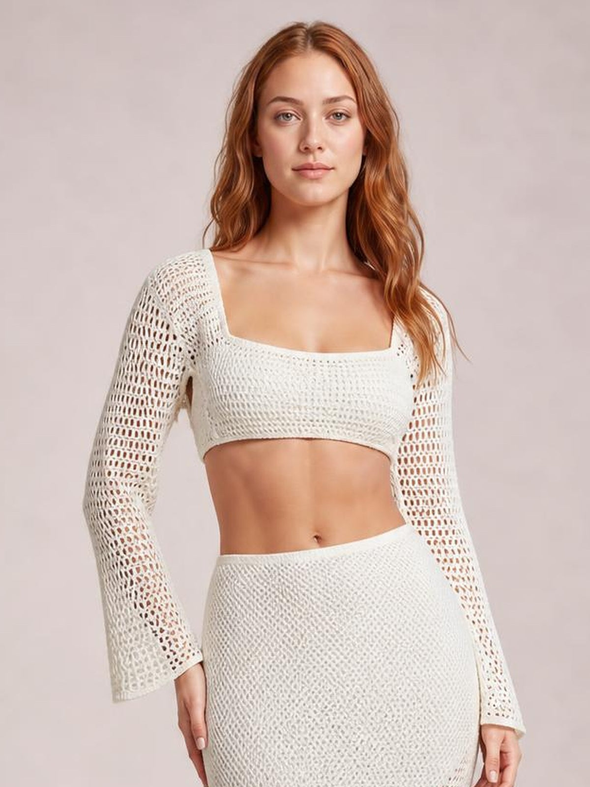 Model stands in a white openwork cover-up set with a square-neck cropped long-sleeve top and fitted high-waisted skirt, showing a sleek silhouette.