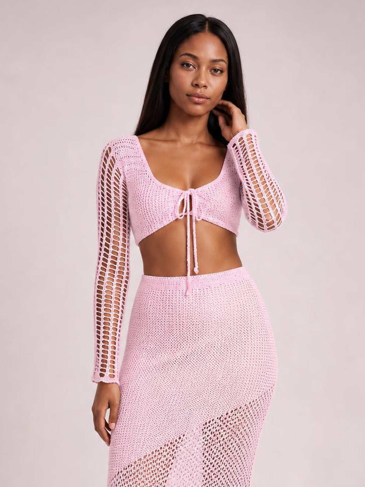 Model poses in a pink tied long sleeve top and skirt cover up set with openwork sleeves, a cropped front tie, and a fitted midi skirt.