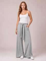 Model wears gray tied pocketed wide-leg pants with a relaxed, flowing silhouette, standing with one hand tucked into a side pocket.