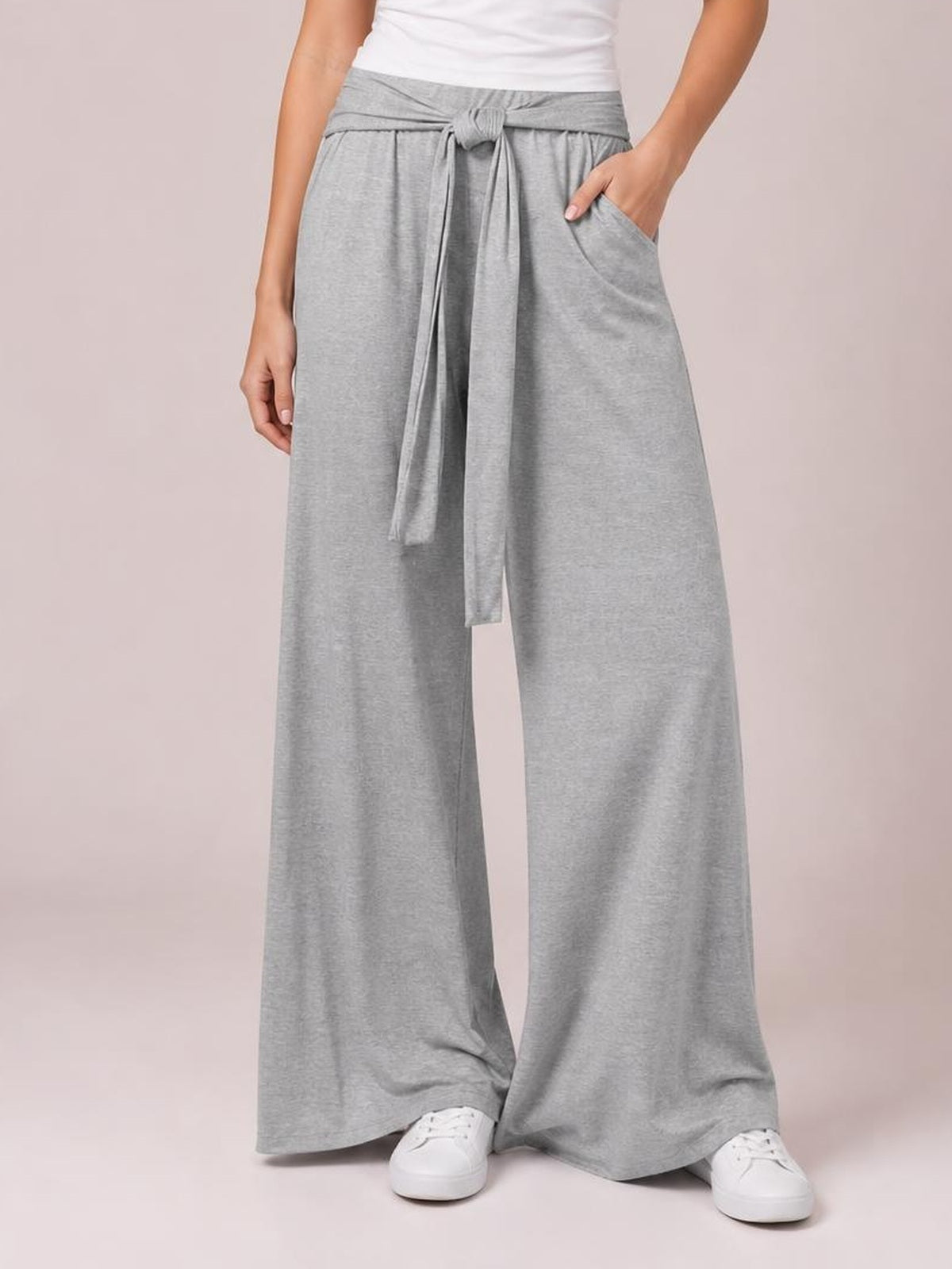 Model wearing light gray tied pocketed wide-leg pants with a relaxed silhouette, gathered waist, long front tie, and hands placed in the side pockets.