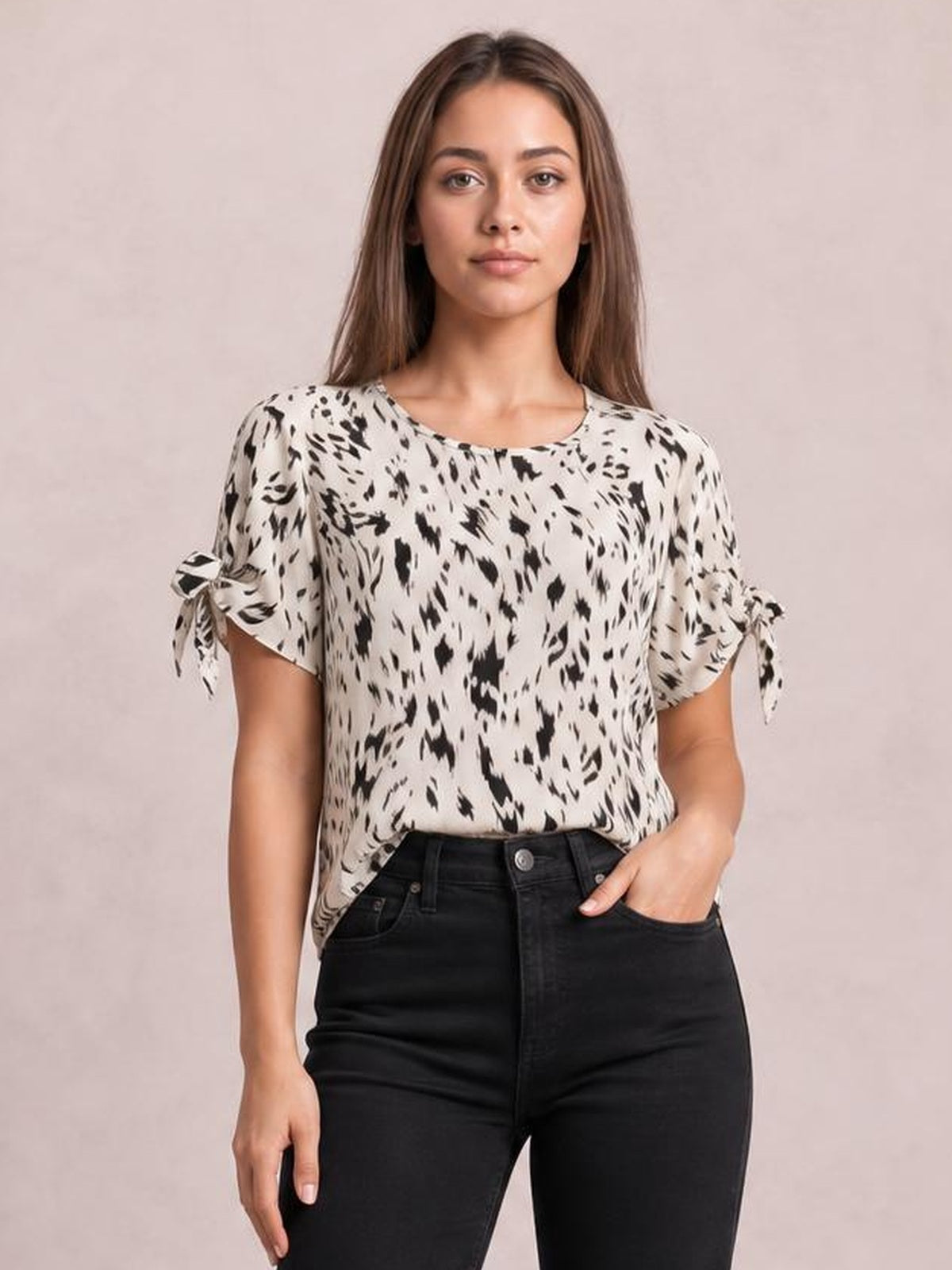 Model wearing an ivory printed boat neck blouse with black abstract pattern, short tied sleeves, and a relaxed straight silhouette, paired with black jeans.
