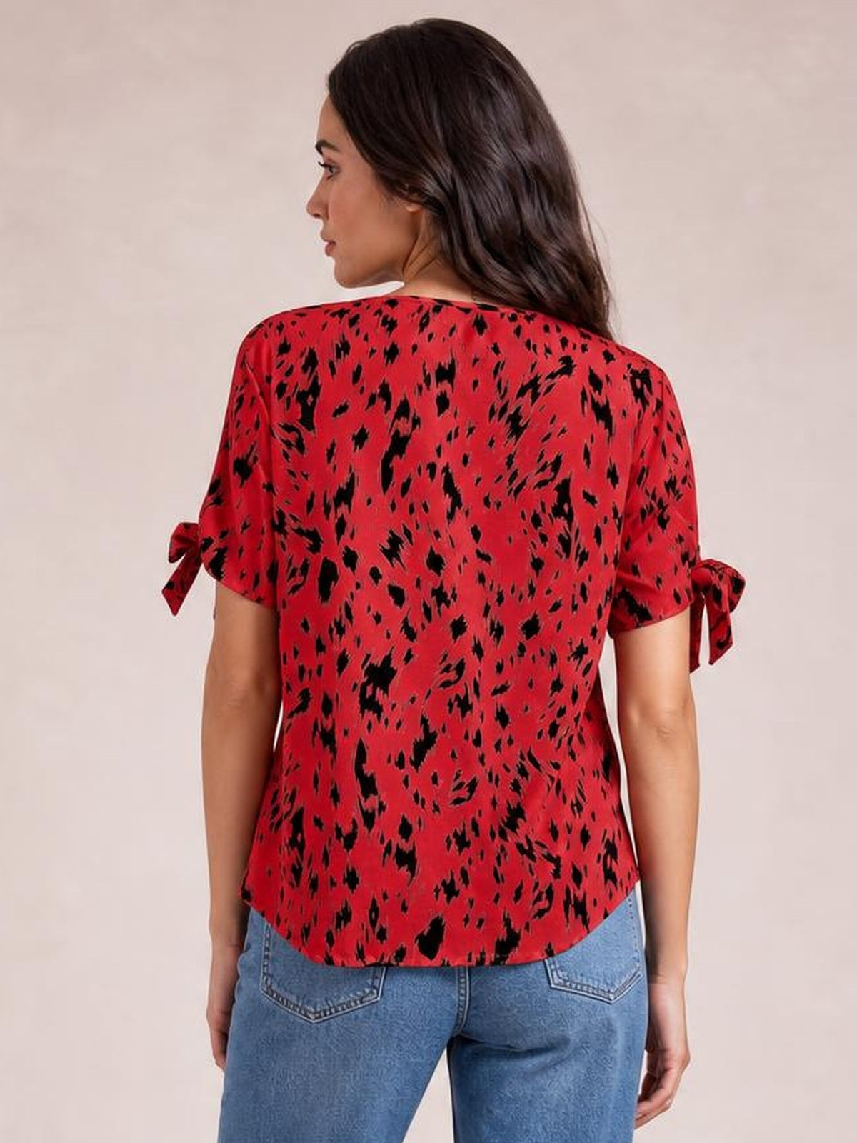 Back view of a model wearing a red and black printed boat neck blouse with short sleeves, tied bow details, and a relaxed straight silhouette.