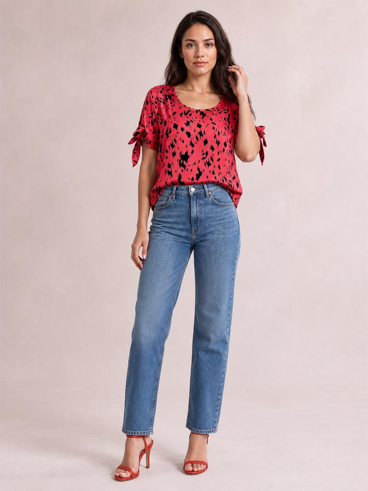 A model poses in a red printed boat neck blouse with a relaxed silhouette and tied short sleeves, paired with straight-leg jeans.