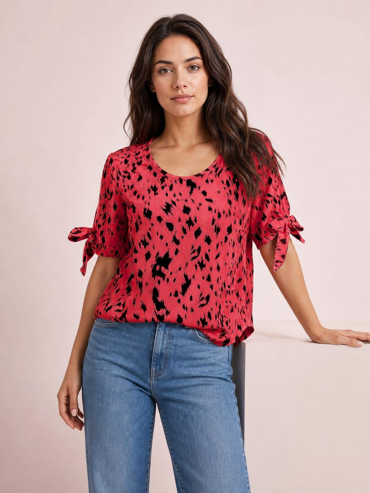Model poses in a pink and black printed blouse with a boat neckline, relaxed silhouette, and short sleeves tied into bows at the sides.
