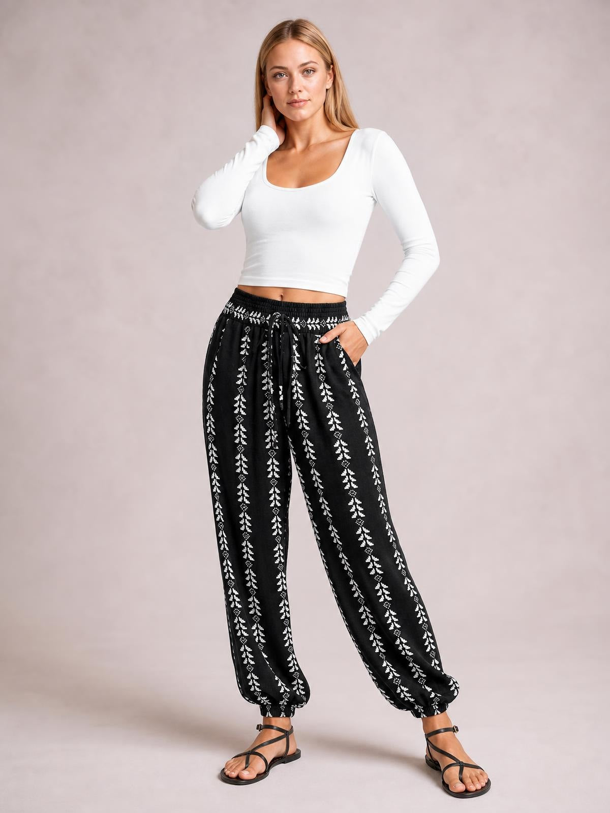 Model poses in black-and-white printed high waist pants with a tied drawstring, relaxed wide-leg silhouette, side pockets, and gathered ankle cuffs.
