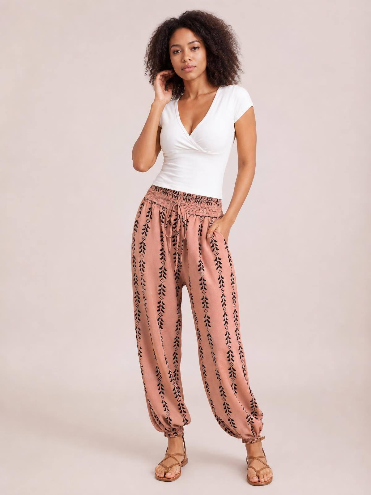 Model poses in pink printed high-waist pants with a tied waistband, black botanical pattern, relaxed wide-leg silhouette, and elasticized ankle cuffs.