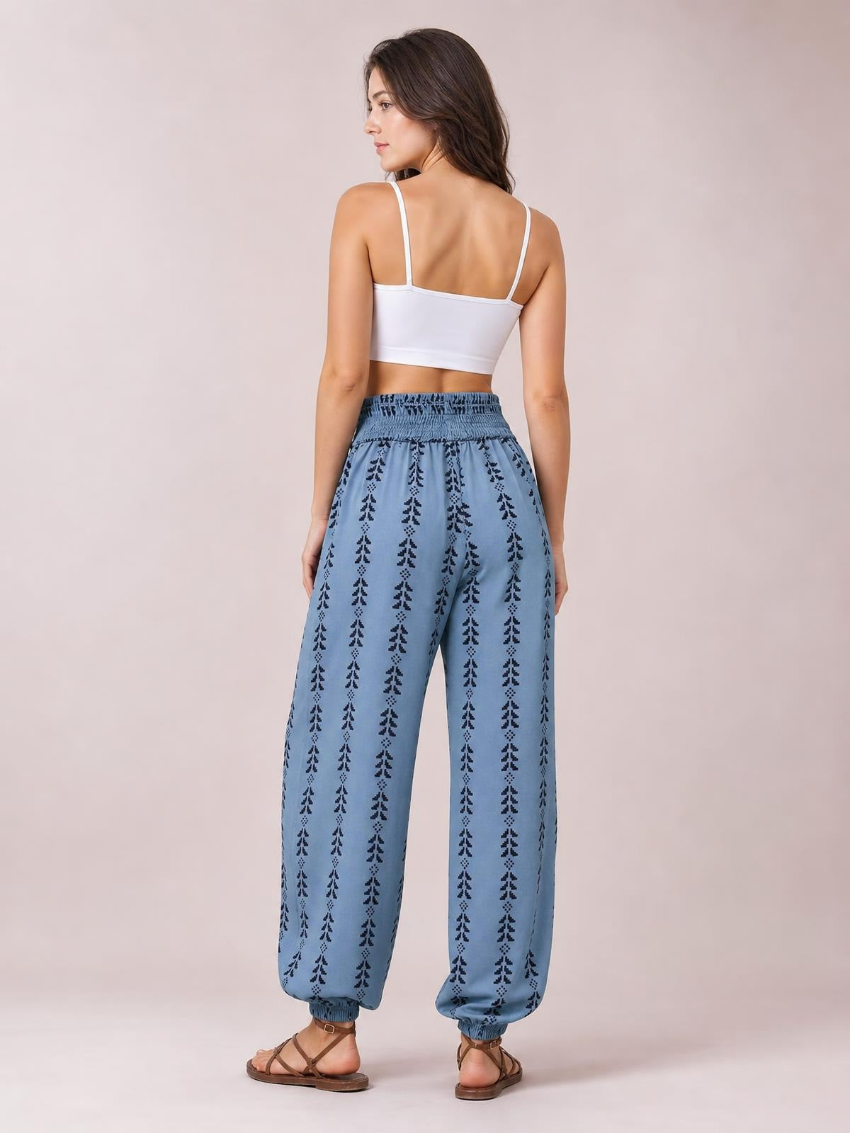 Model poses from the back in blue printed high waist pants with a tied, gathered waistband, relaxed wide-leg silhouette, and elastic ankle cuffs.
