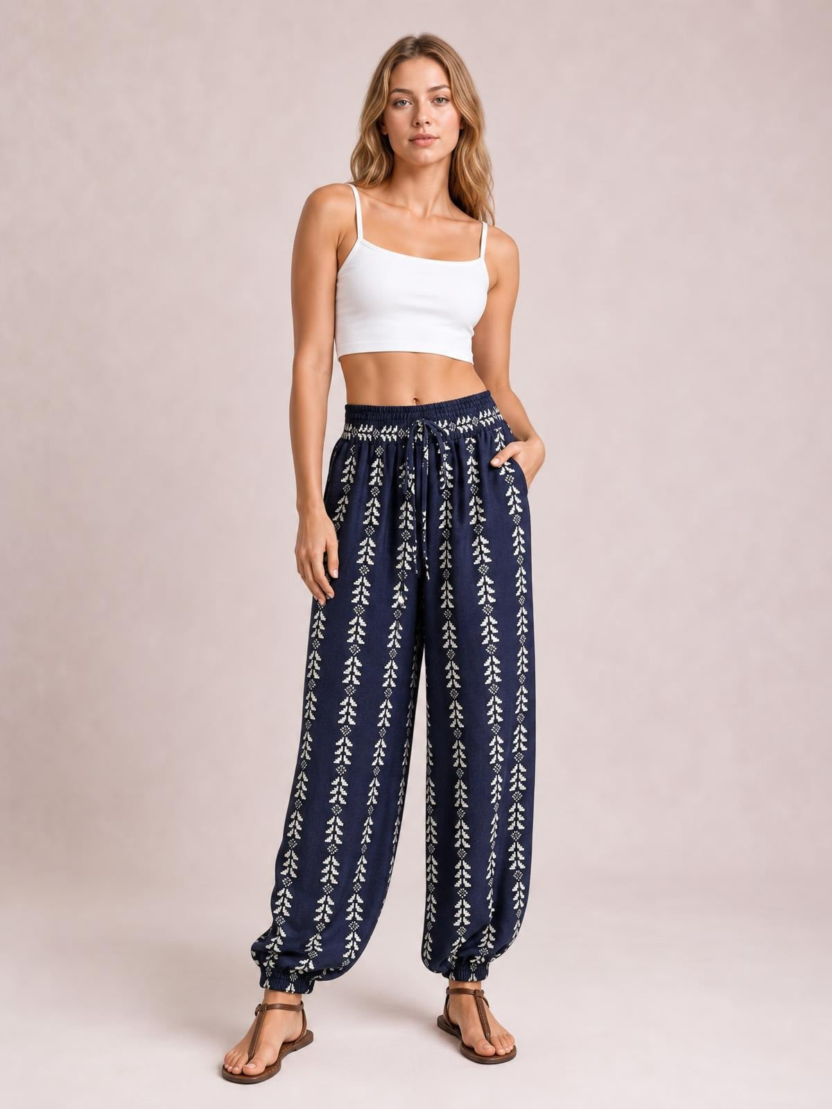 Model poses in navy printed high waist pants with a tied drawstring waist, relaxed wide-leg silhouette, and gathered ankle cuffs.