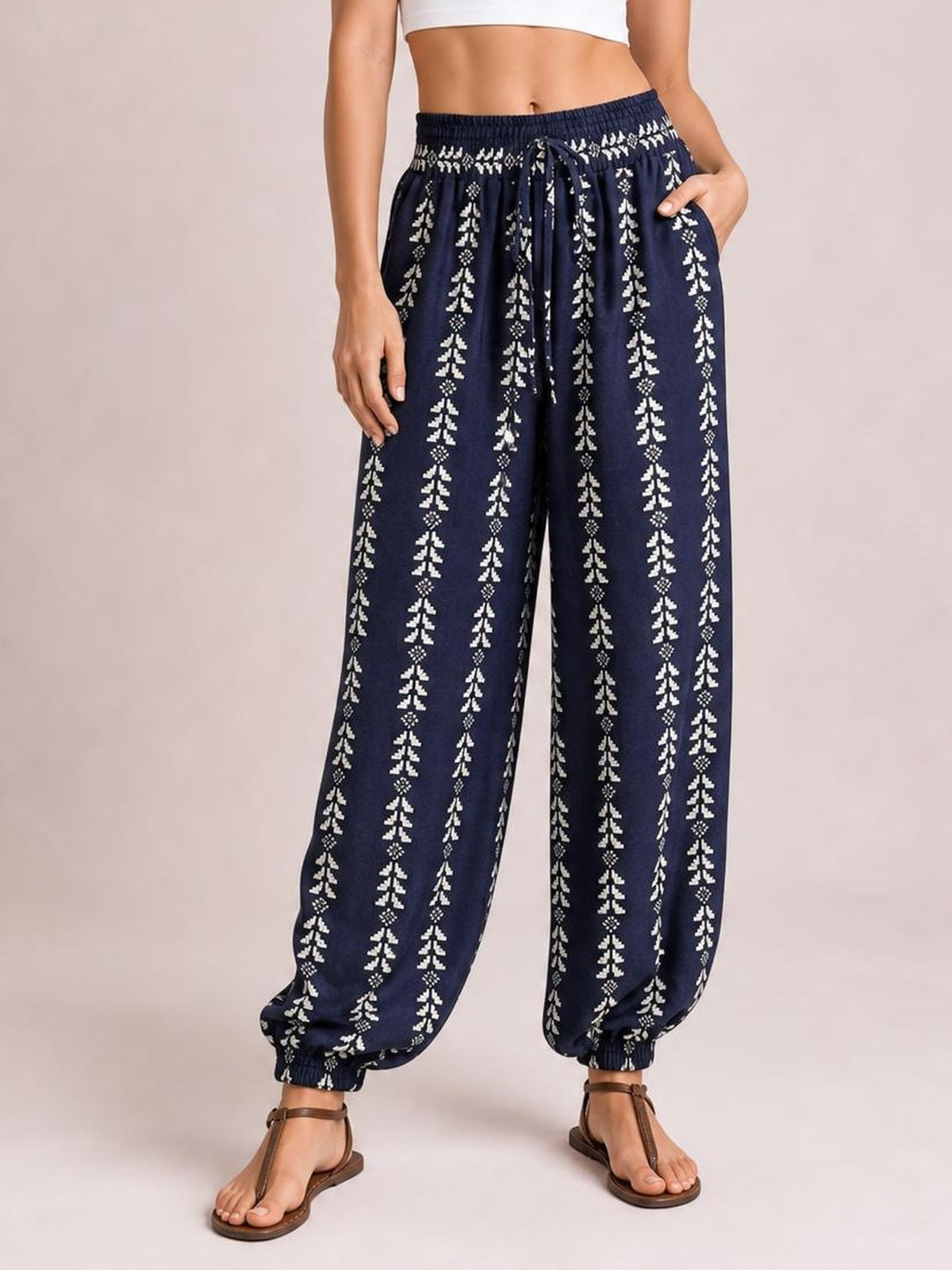 Model wearing navy printed high-waist pants with a tied drawstring, relaxed wide-leg silhouette, side pockets, and elastic cuffs.