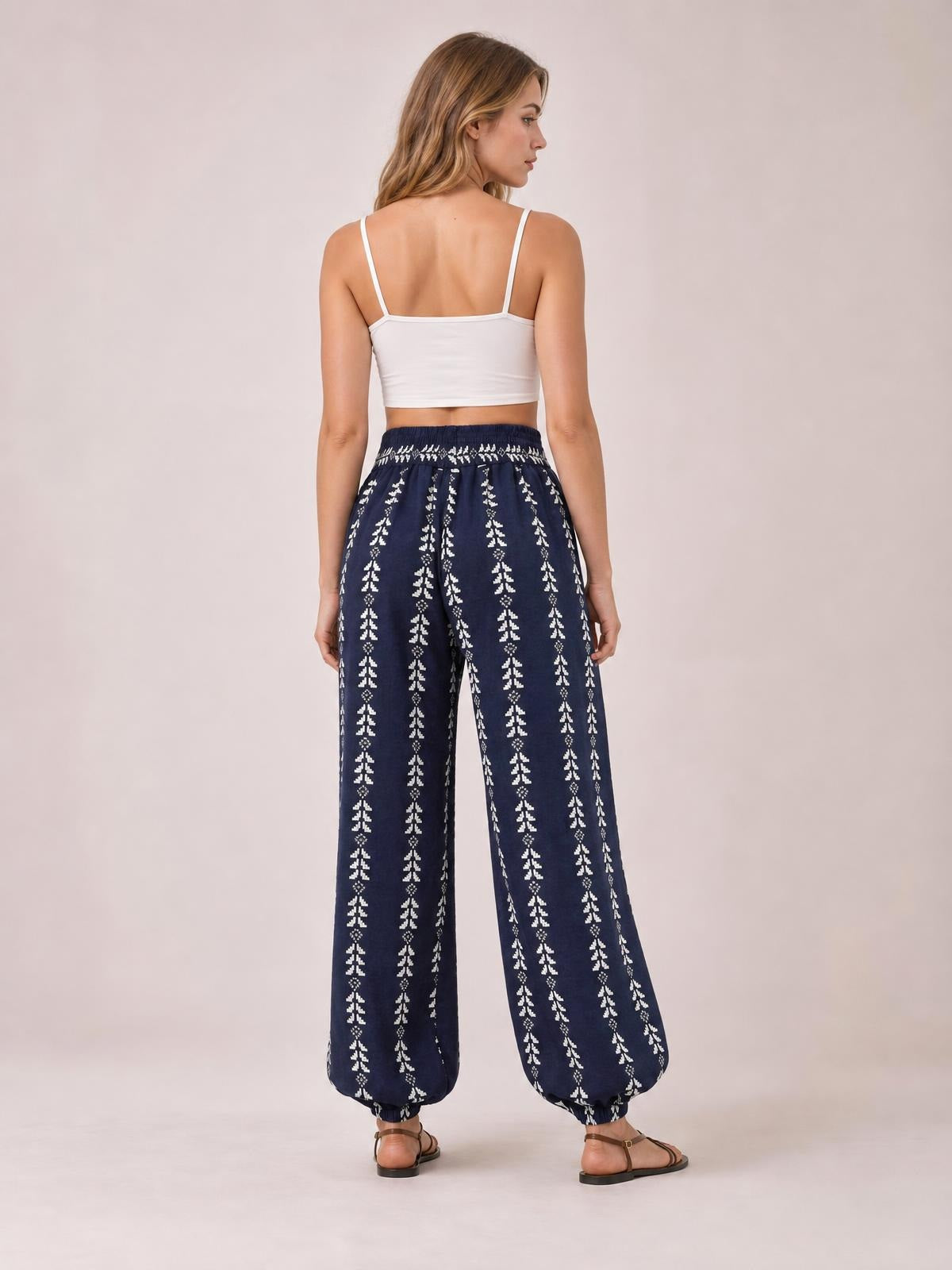 Model poses turned away in navy printed high-waist pants with a wide balloon-leg silhouette, vertical white motifs, and gathered ankle cuffs.