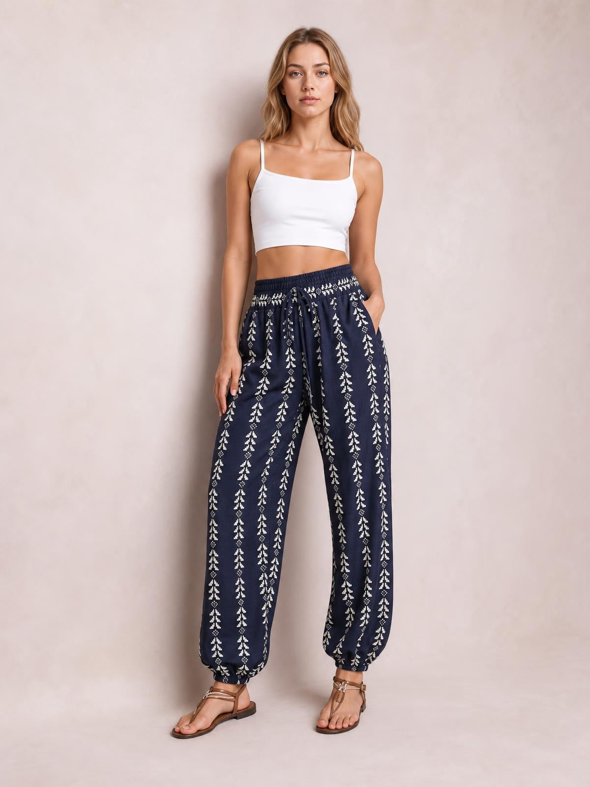 A model stands in navy printed high-waist pants with a tied drawstring waist, relaxed wide legs, and elasticized cuffs, one hand in a pocket.