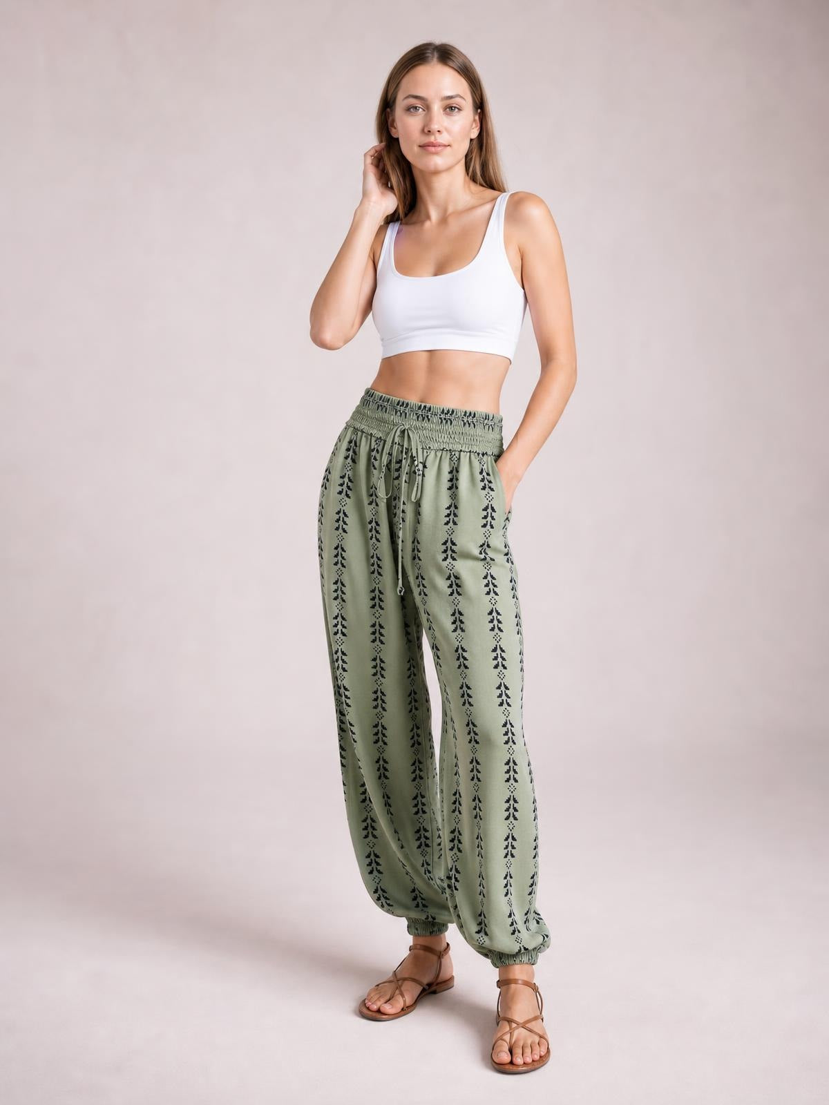 Model poses in sage green printed high waist pants with a tied drawstring waist, relaxed wide-leg silhouette, and gathered ankle cuffs.