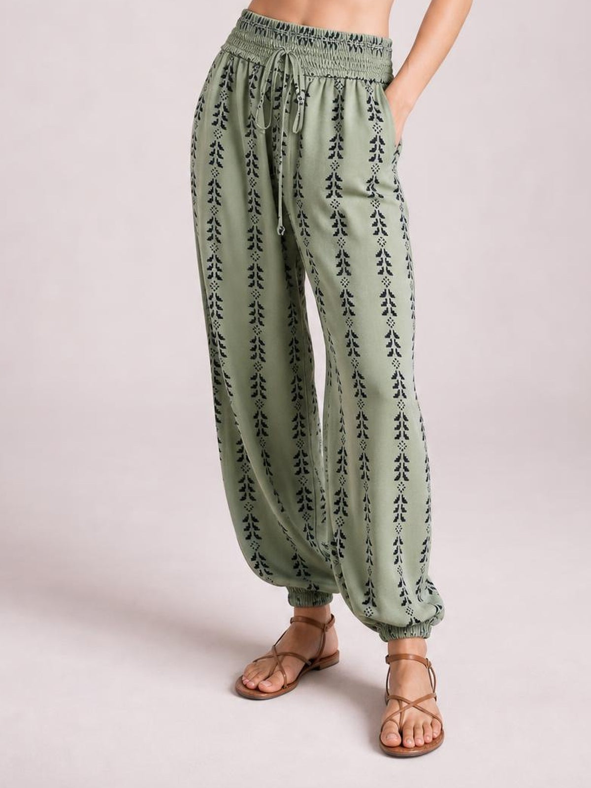 Model wearing sage green printed high-waist pants with a tied drawstring waist, relaxed wide-leg silhouette, and elasticated ankle cuffs.