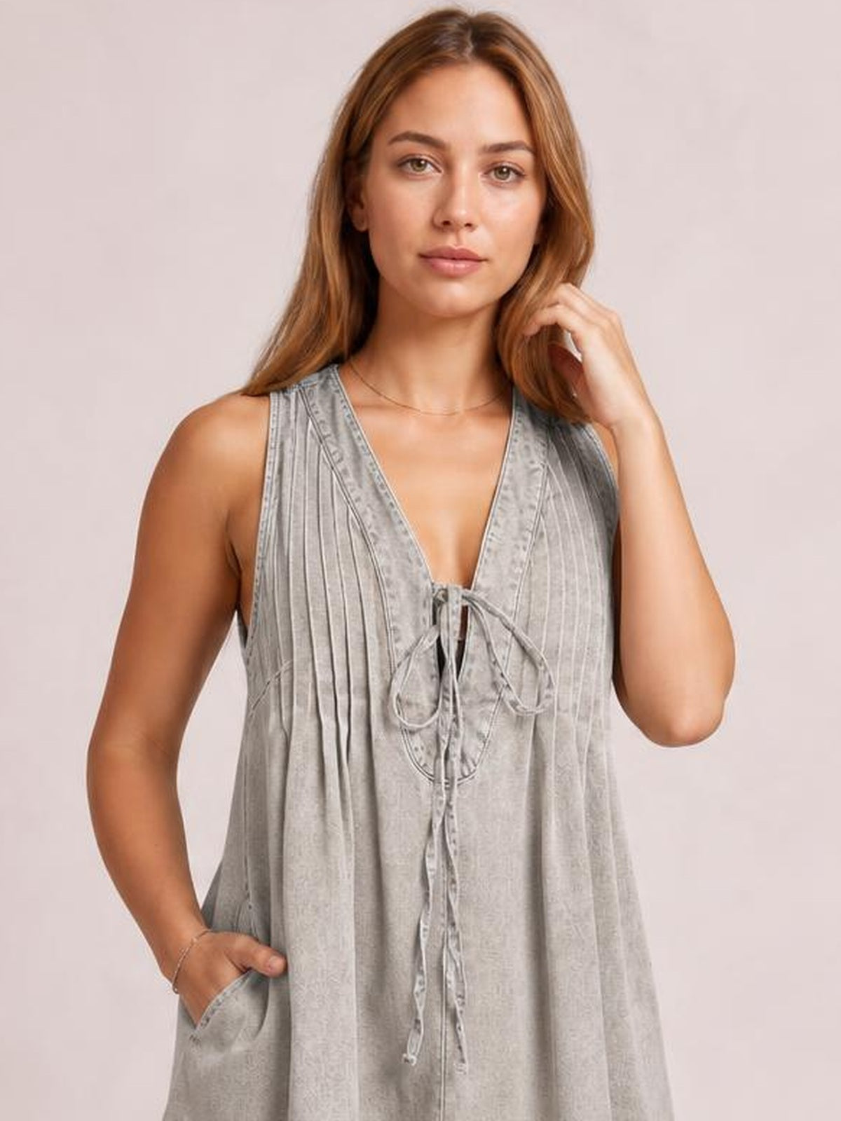 Model poses in a loose gray striped romper with a deep V-neck, tied front, sleeveless construction, and a visible side pocket.