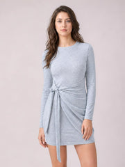 Model stands in a light gray tied mini dress with a round neckline, long sleeves, fitted silhouette, and draped wrap-style waist detail.