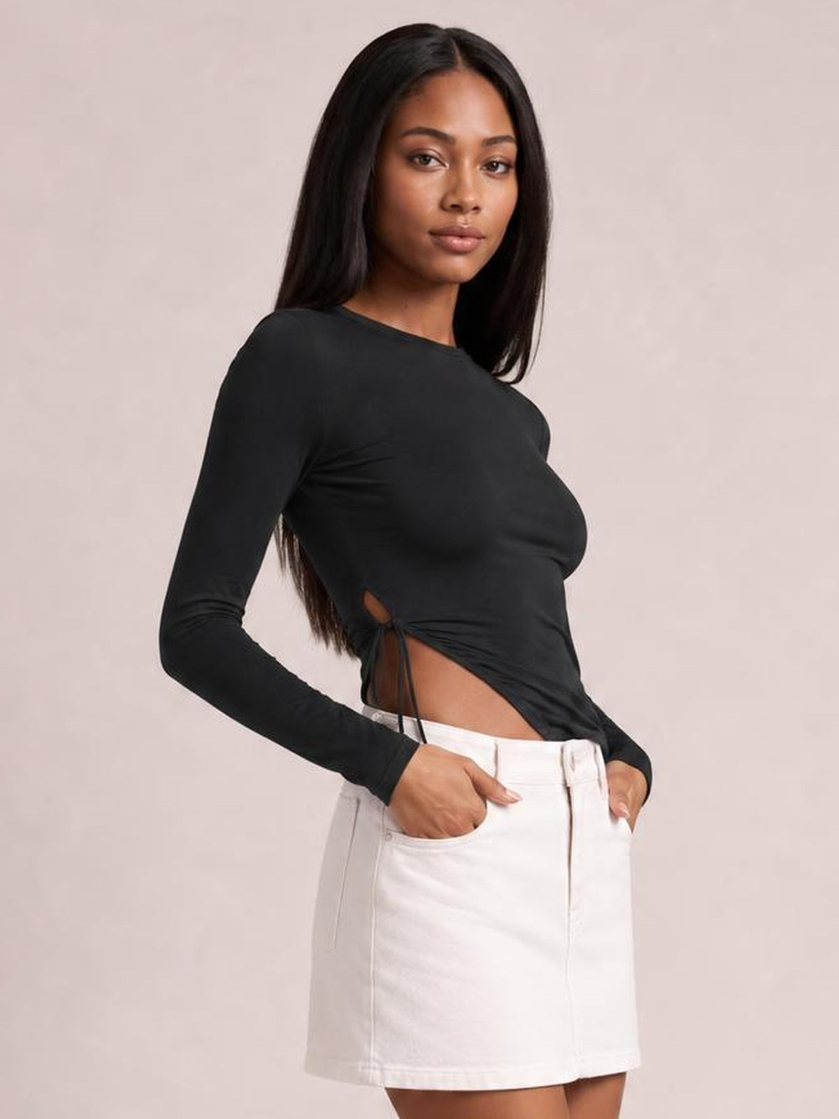 A model poses with hands in pockets wearing a black round-neck long-sleeve T-shirt with a fitted silhouette, side slit, and tied waist detail.