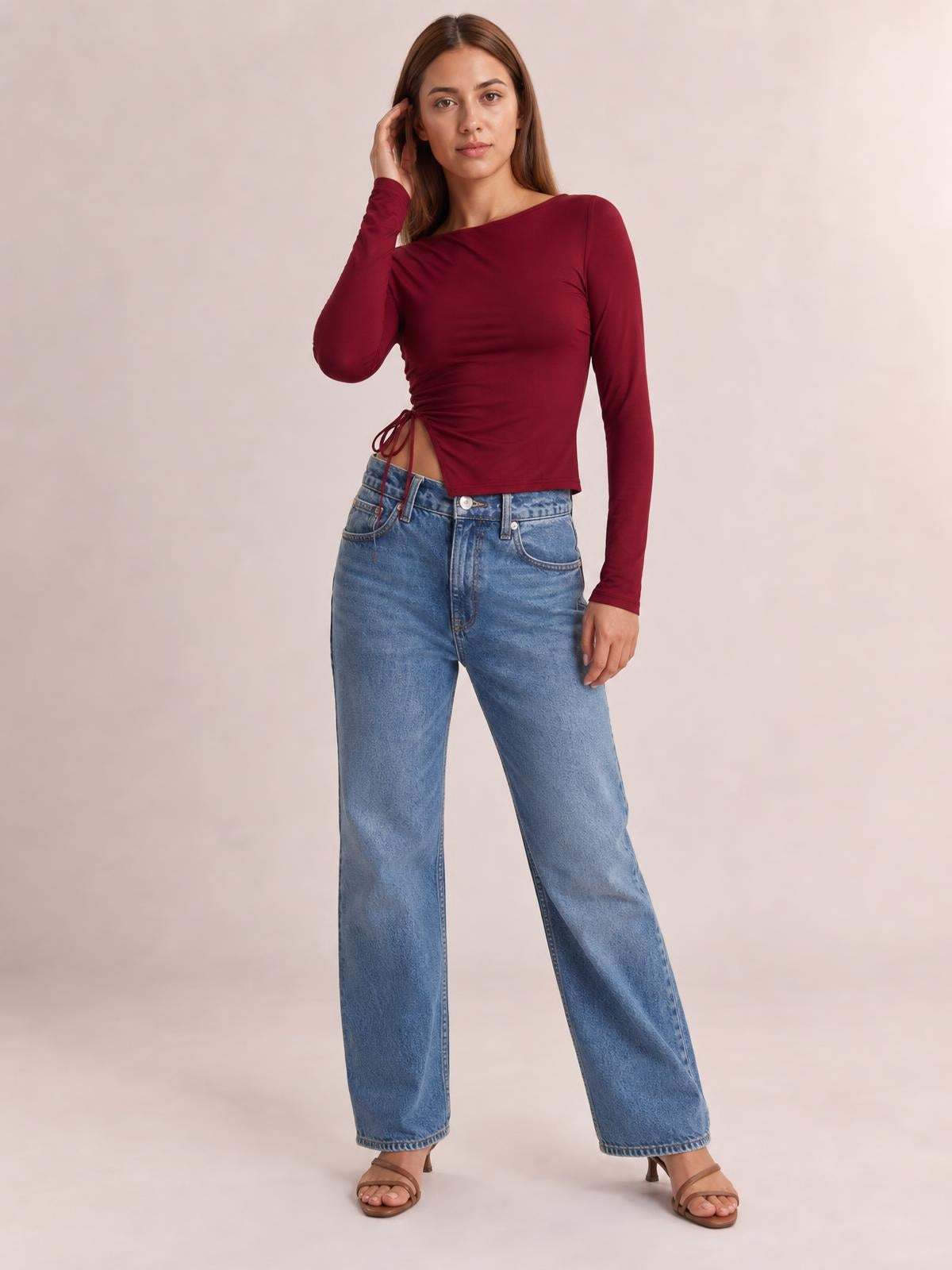A model poses in a burgundy long-sleeve T-shirt with a round neck, fitted cropped silhouette, and tied side slit detail creating subtle ruching.