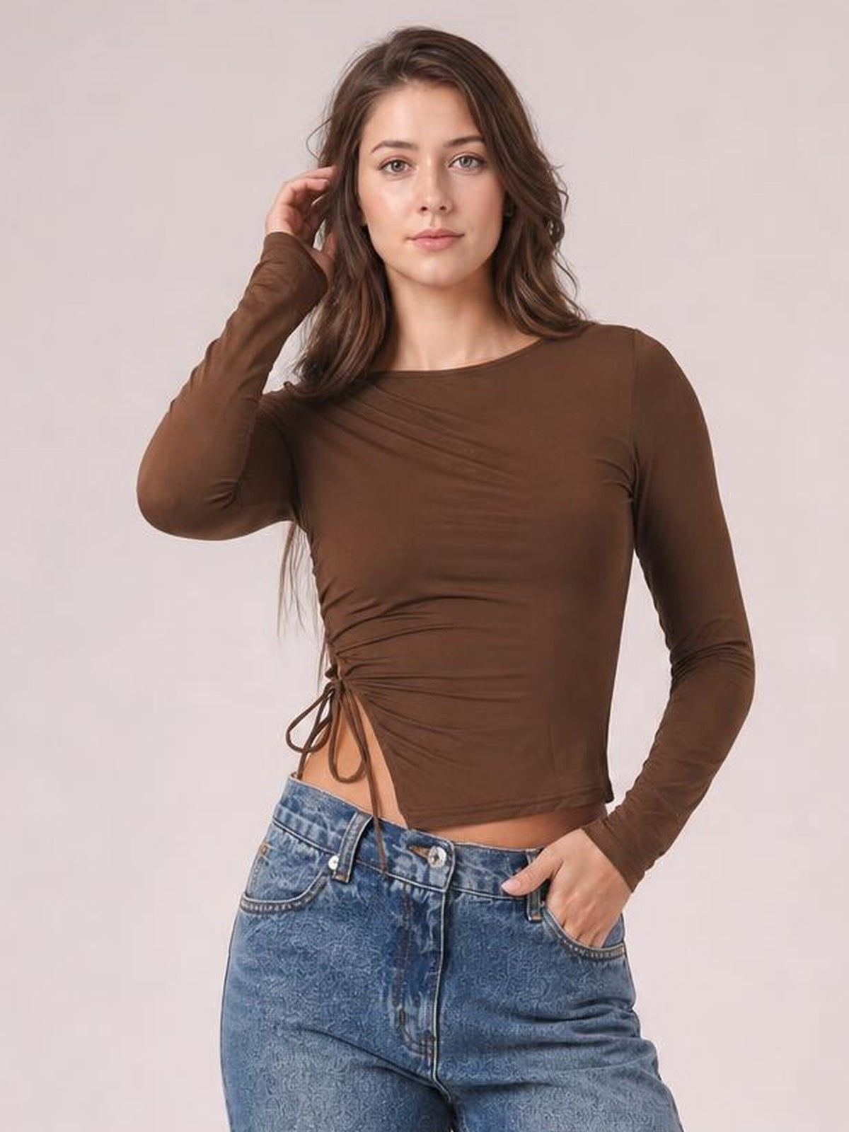 Model wearing a brown tied slit round neck long sleeve T-shirt with a fitted silhouette, ruched side detail, and drawstring opening at the waist.
