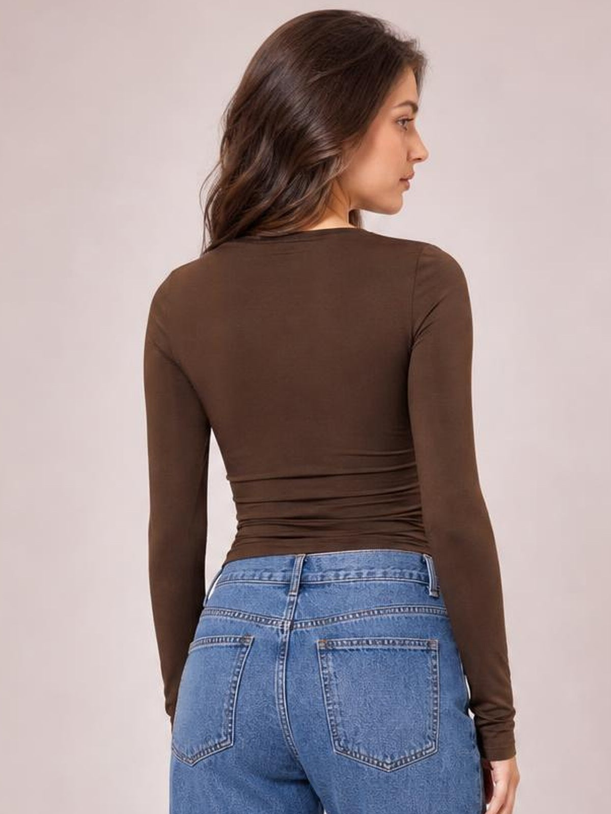 A model looks over her shoulder wearing a fitted brown round-neck long-sleeve T-shirt with a softly gathered waist and smooth stretch silhouette.
