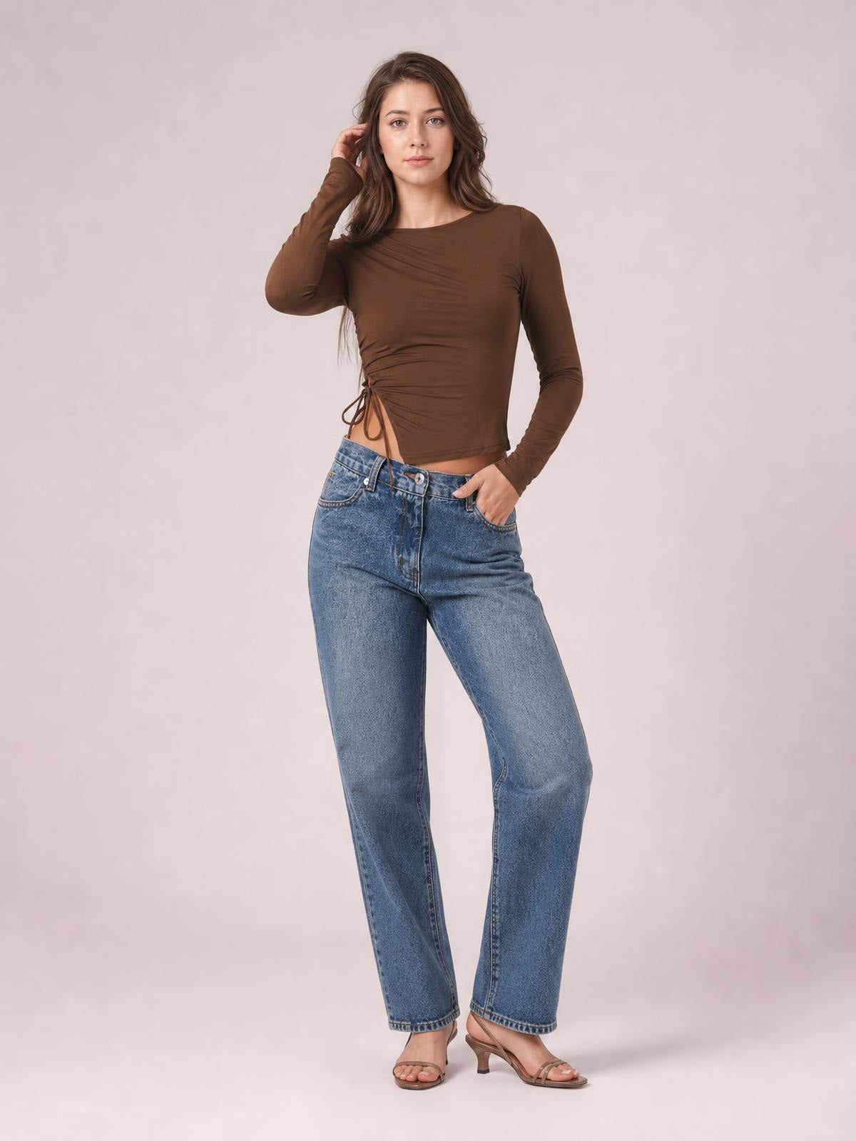 A model poses in a fitted brown tied slit round neck long sleeve T-shirt with ruched waist detailing and a cropped silhouette, hand in pocket.